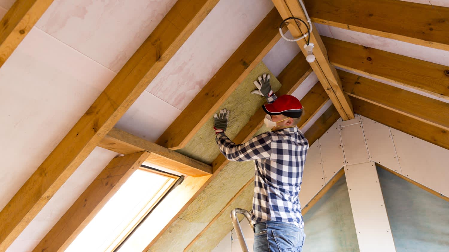 A man installing thermal roof insulation on a house’s attic