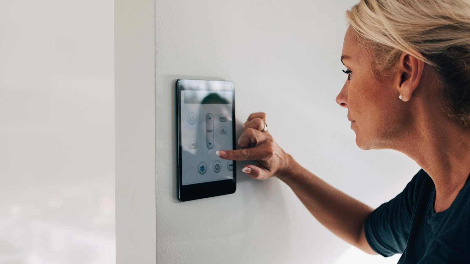 A woman adjusting the temperature via a smart thermostat