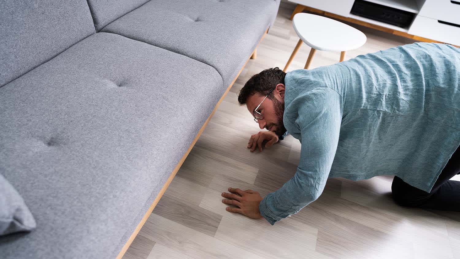 man looking for something under a couch