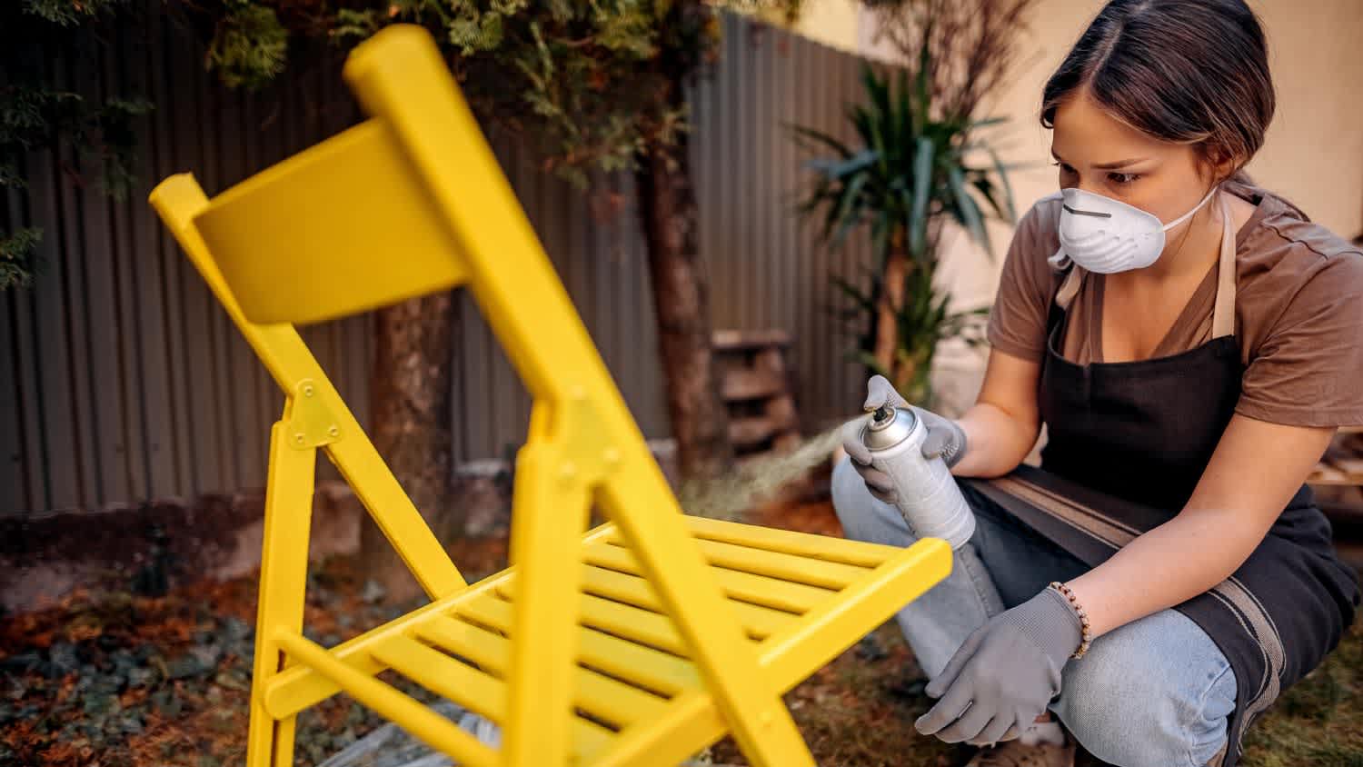 A woman painting furniture in backyard of her home