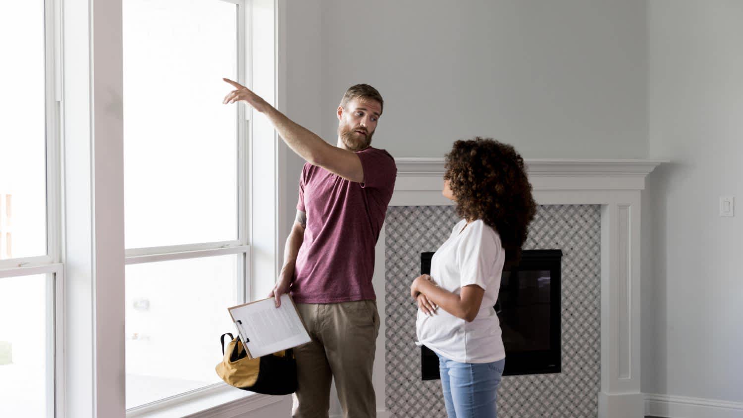 A home inspector points to something outside while talking with homeowner