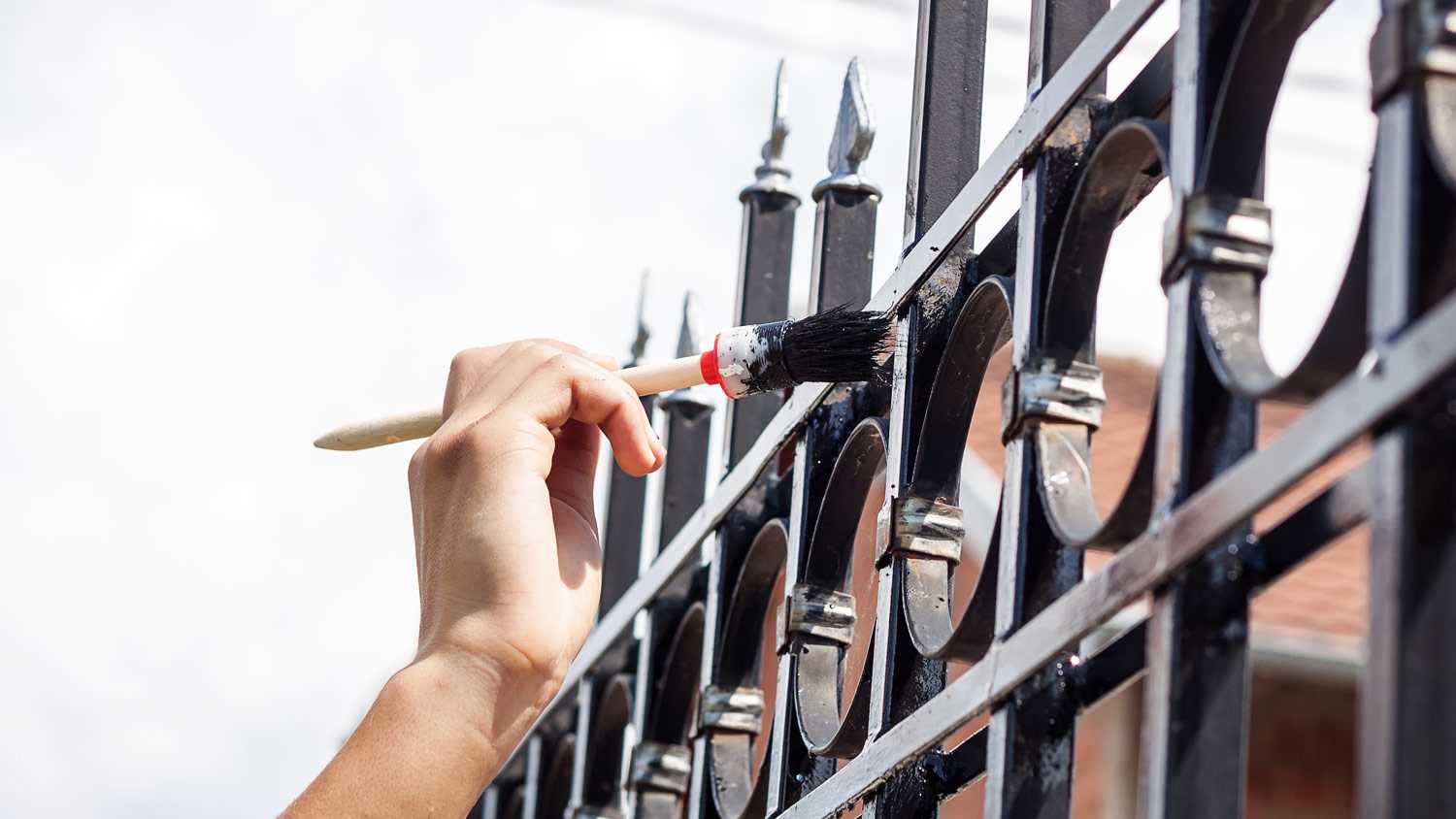 A hand using a brush painting a metal fence