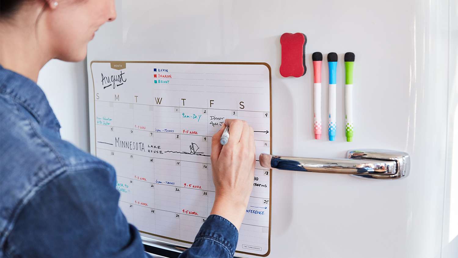woman filling out family calendar on fridge