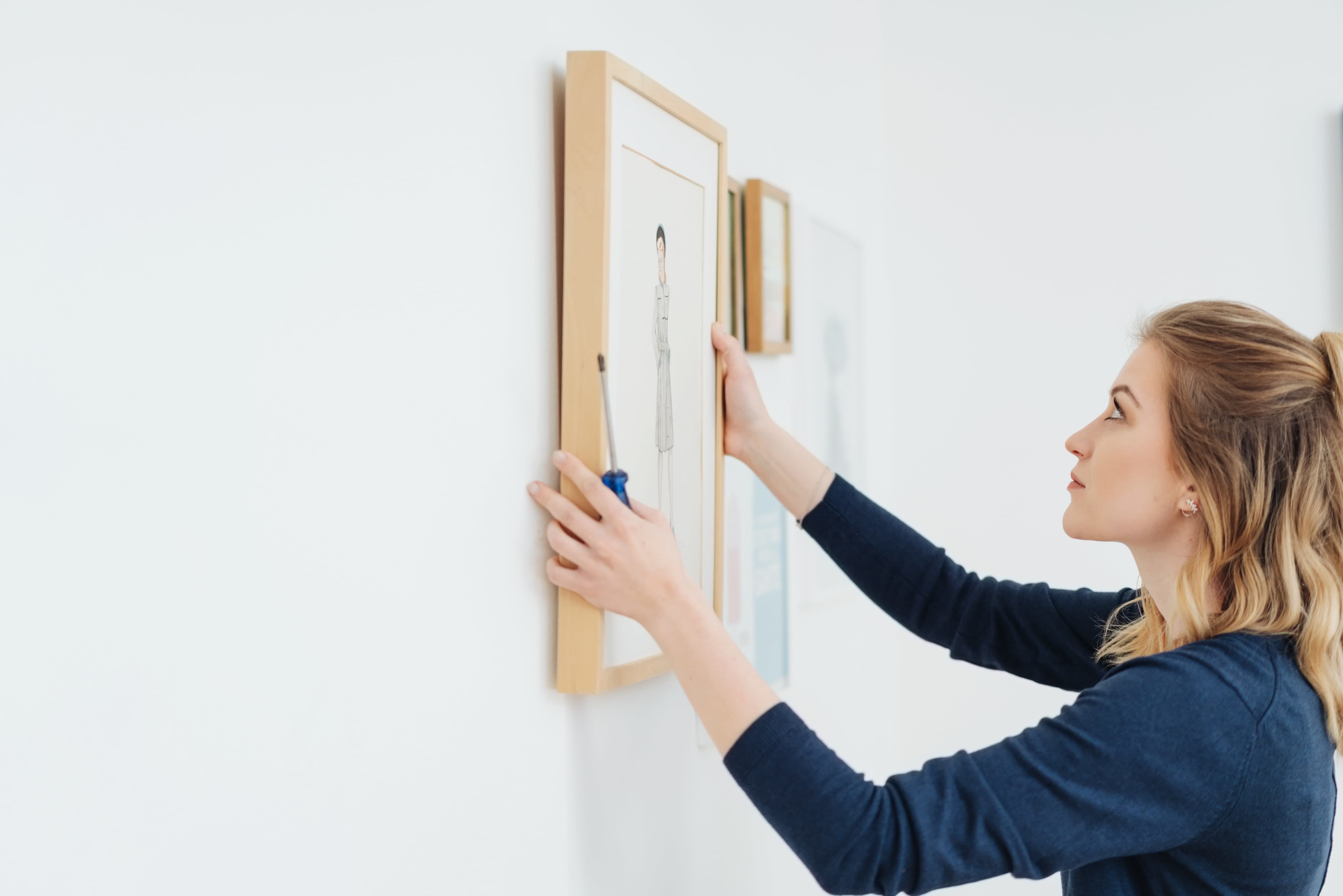 Young woman hanging a picture on the wall at eye level