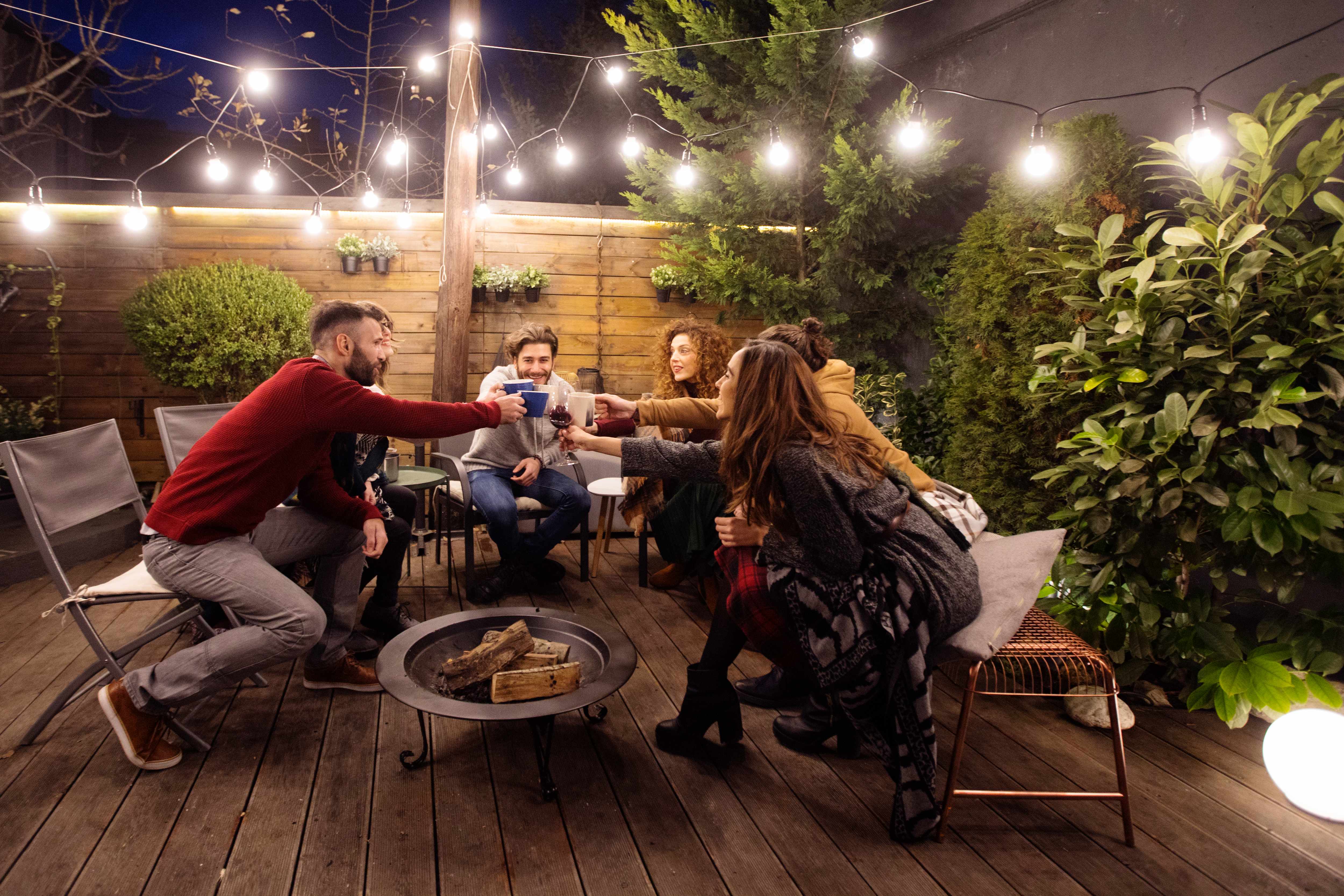 Friends sitting around a fire pit under string lights
