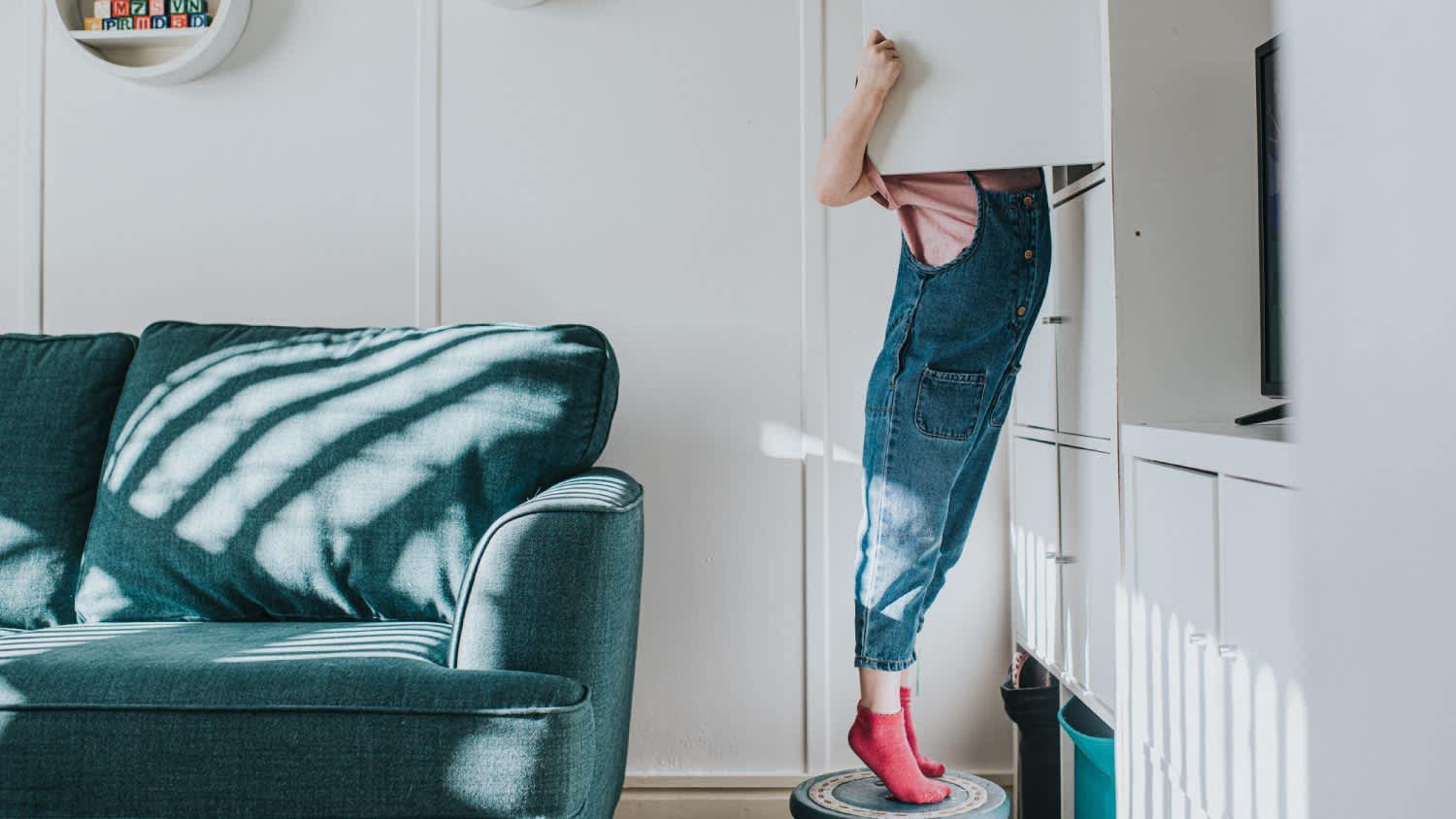 A girl stands on her tip-toes on a little stool to open a cabinet