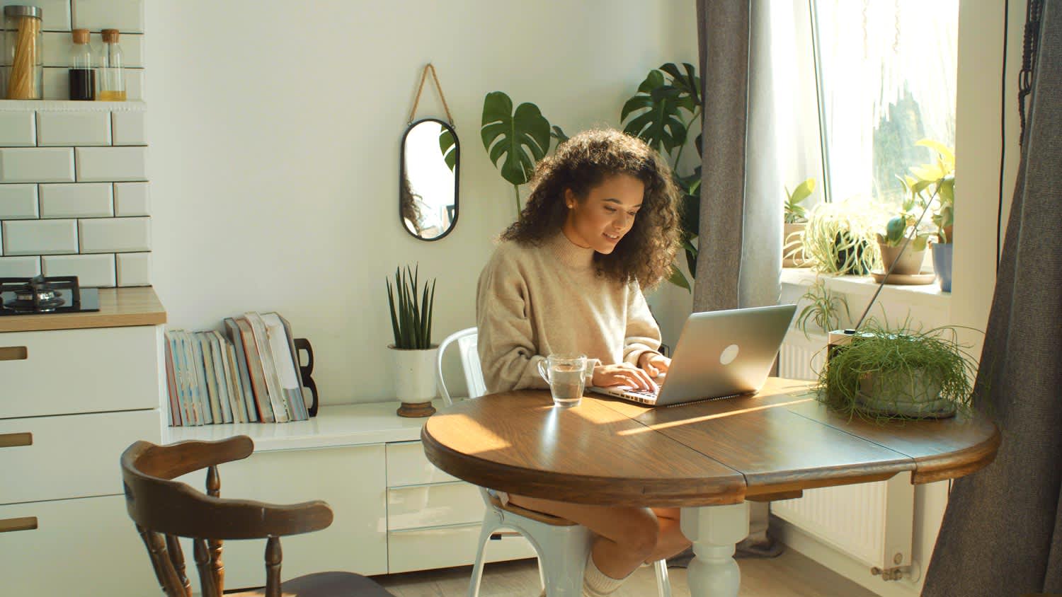A young woman surrounded by plants using her laptop in her house