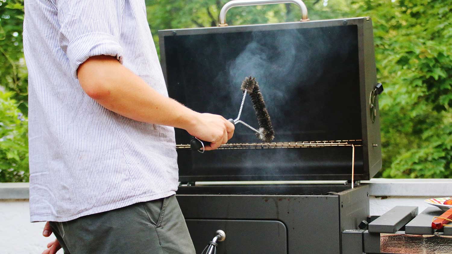 Man holding wire brush is cleaning barbecue grill