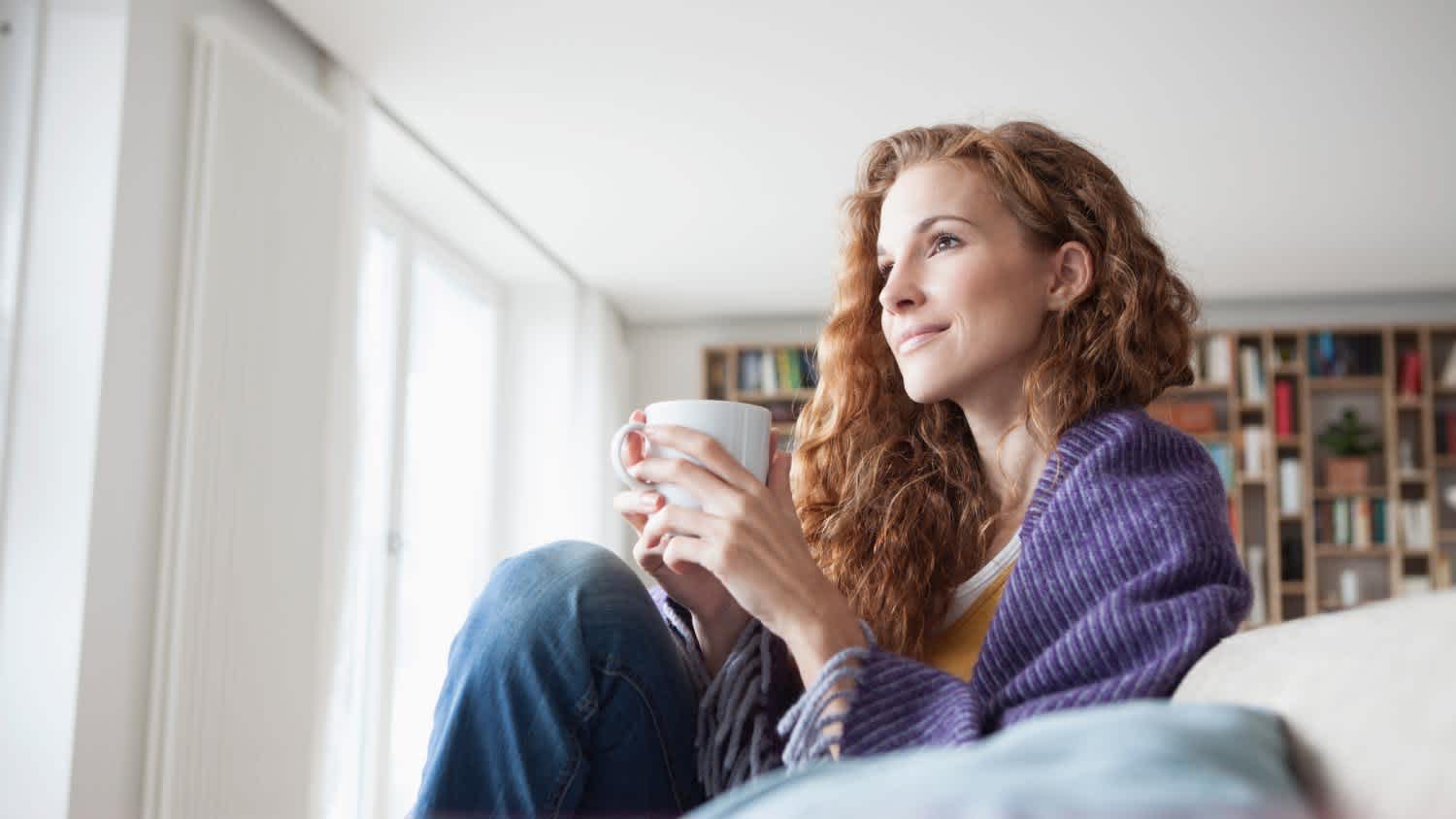 A woman at home sitting on couch holding cup