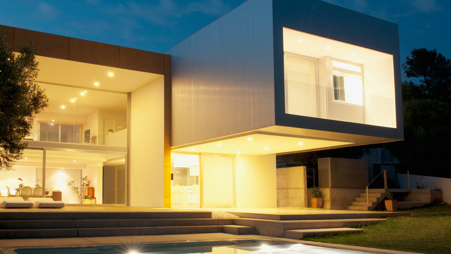 The exterior of a modern house with a pool at night