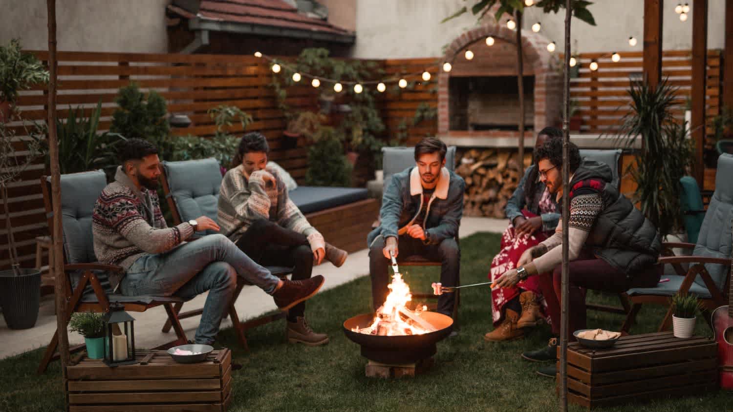 Friends hanging out by fire pit in backyard