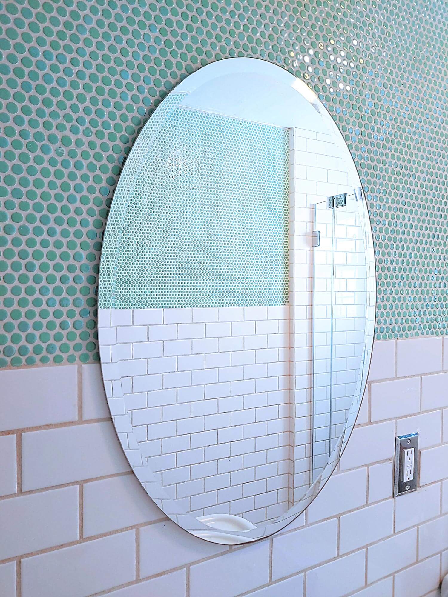 A big mirror with aqua penny tiles on the wall