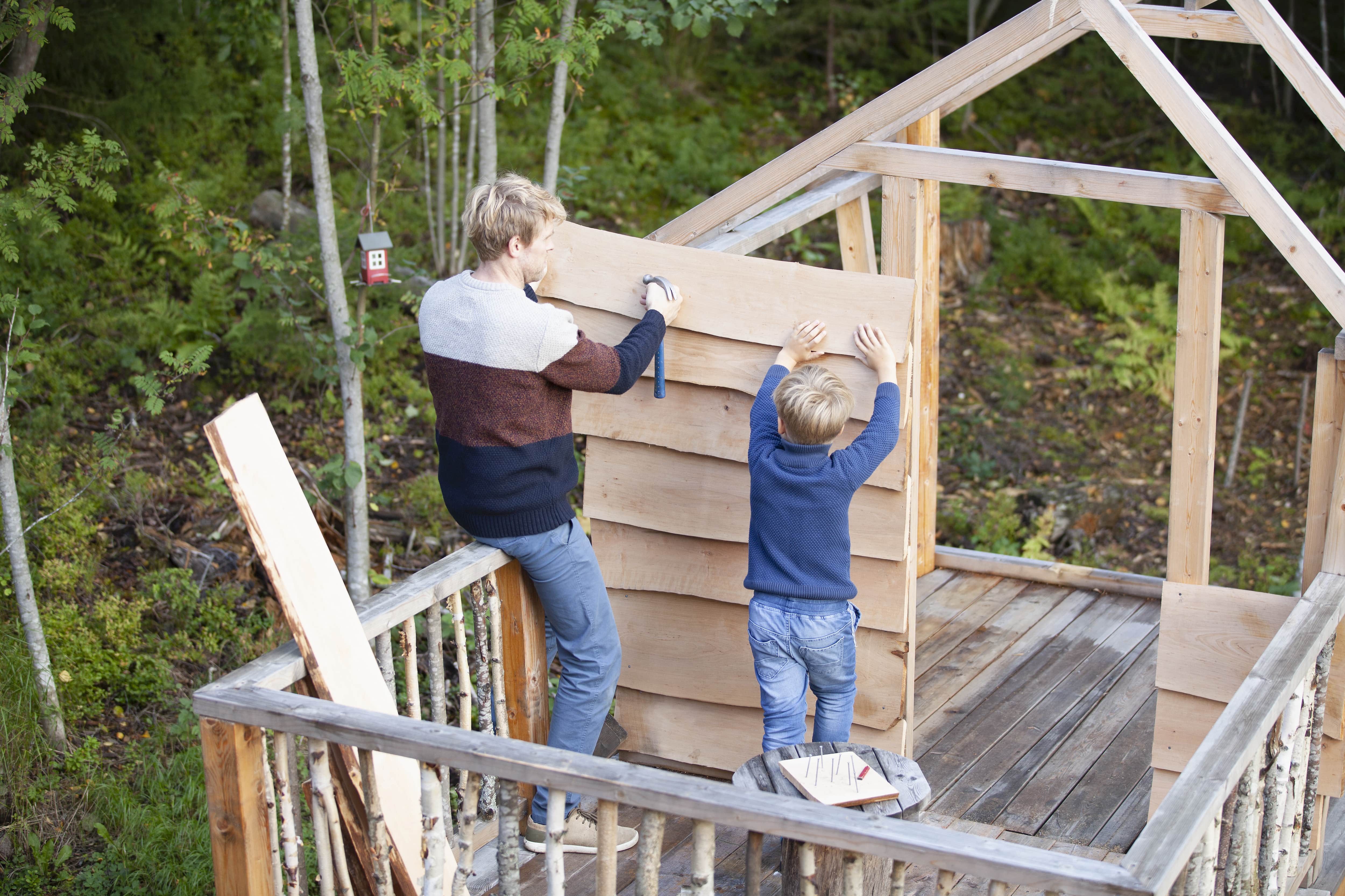 A father and son installing siding to a treehouse