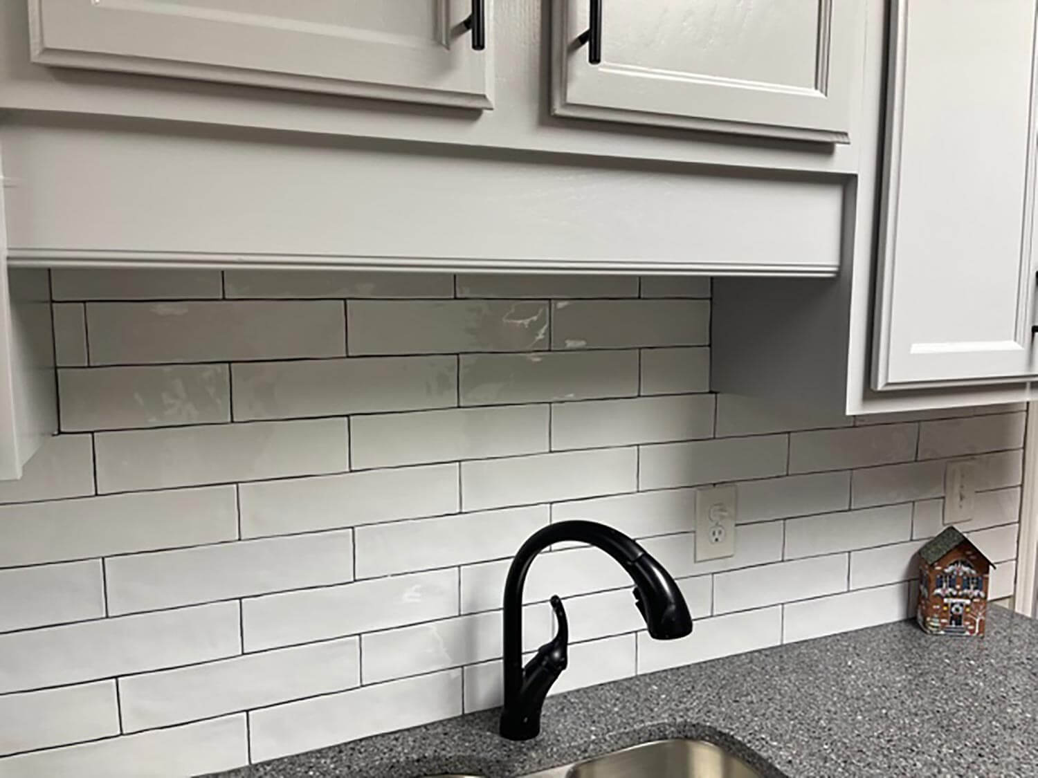 A kitchen sink with glossy white tiles on the wall