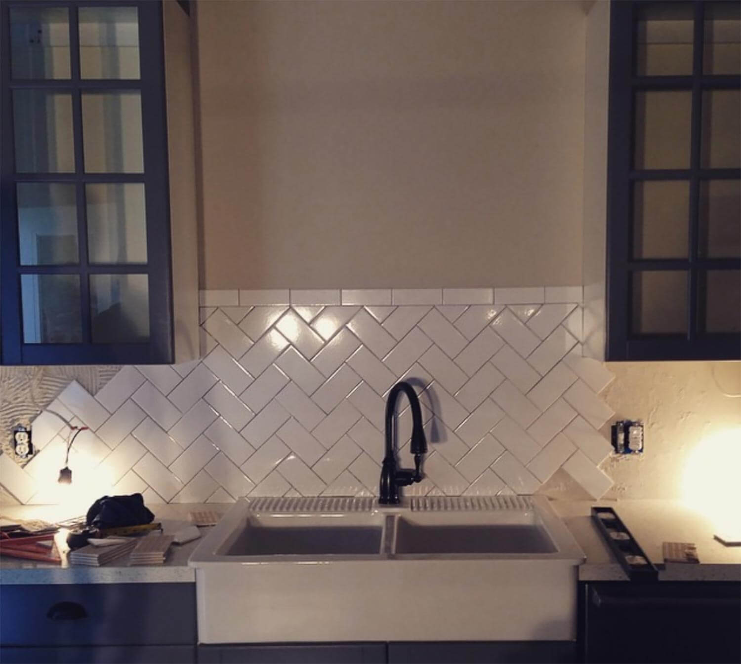 A kitchen sink with herringbone styled subway tiles on the backdrop