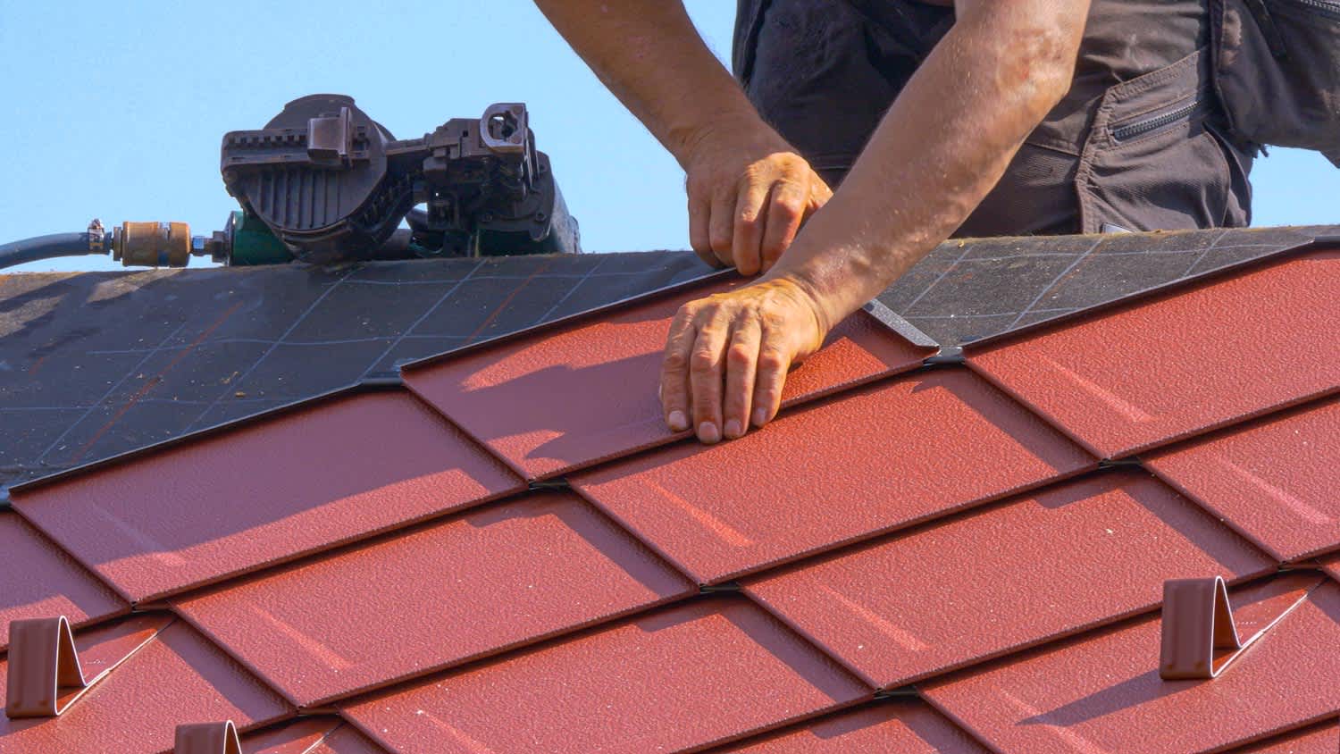 A worker laying new aluminum shingles on the roof