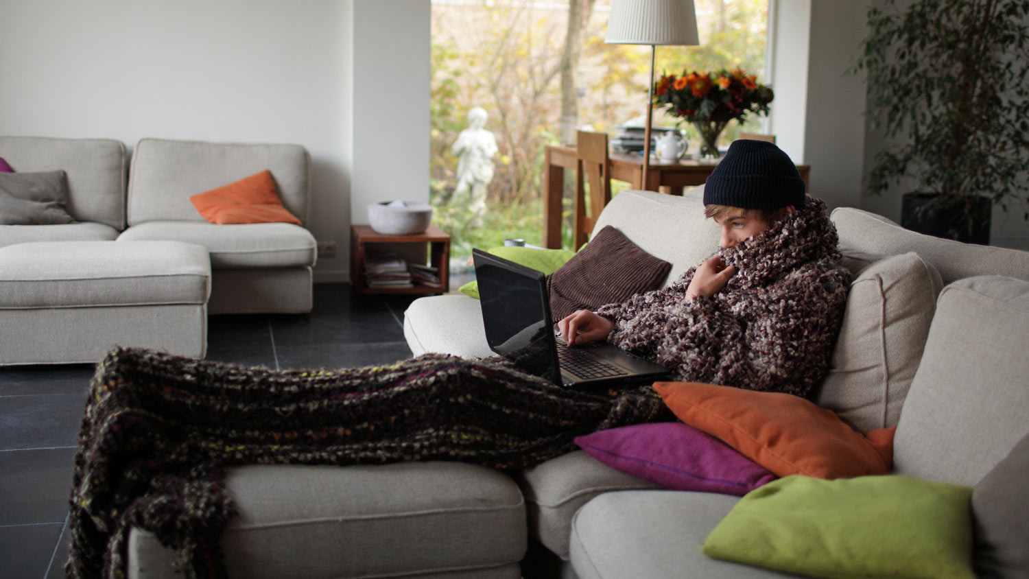 A young man under a blanket working on his laptop