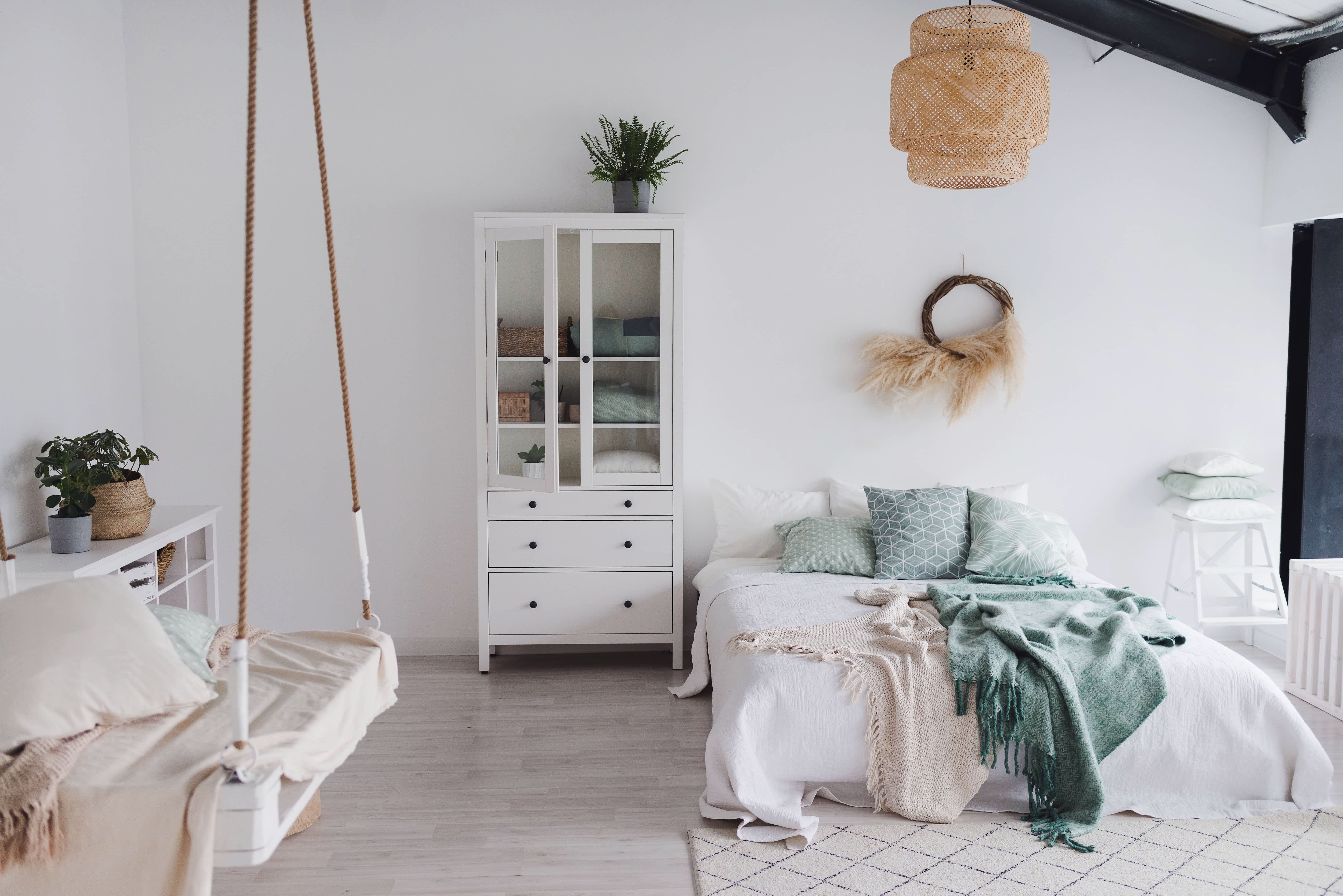 Sunny bedroom with white bedding and walls, platform swing, wheat wreath, and rattan chandelier