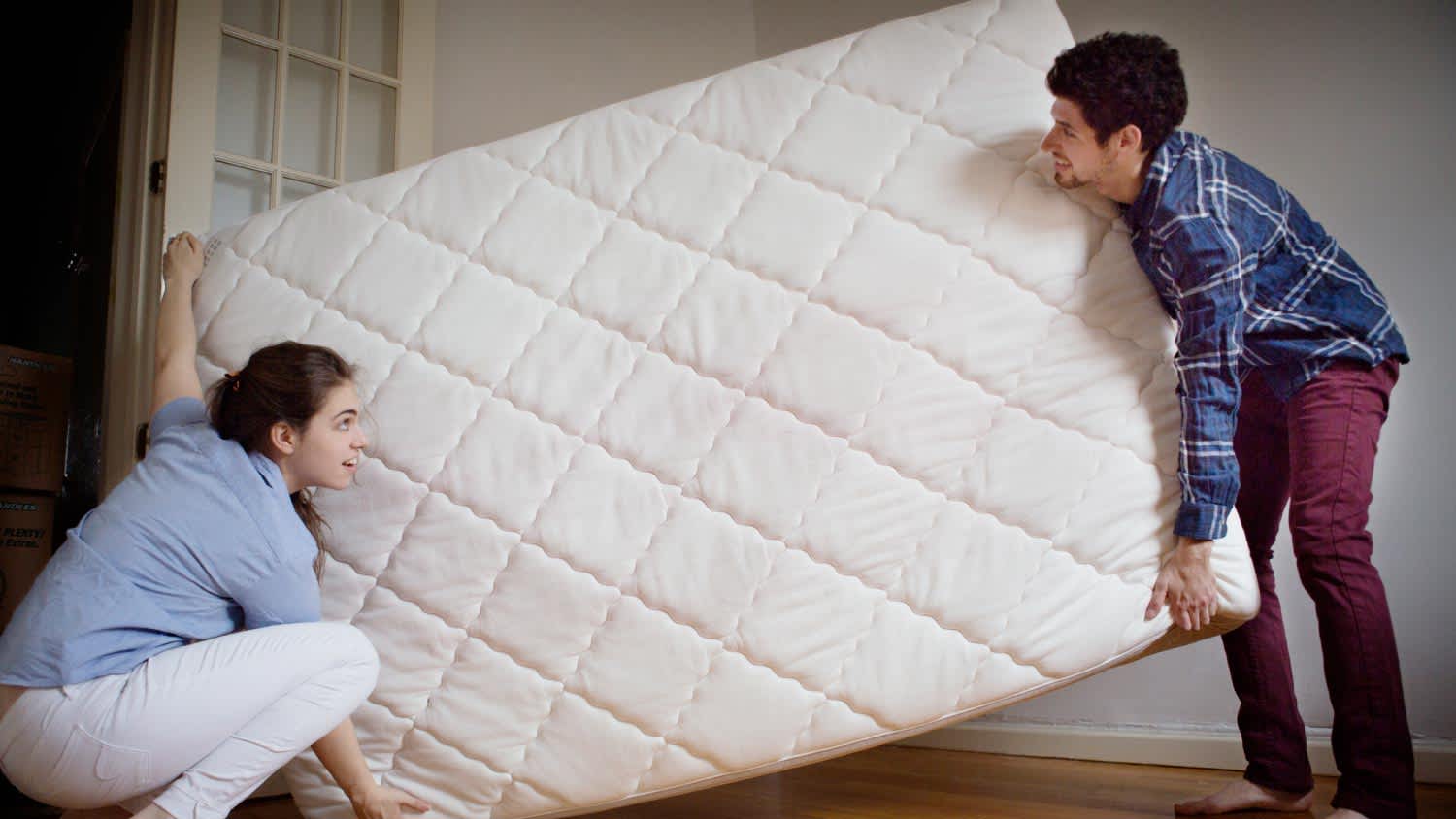 Couple carrying mattress in room