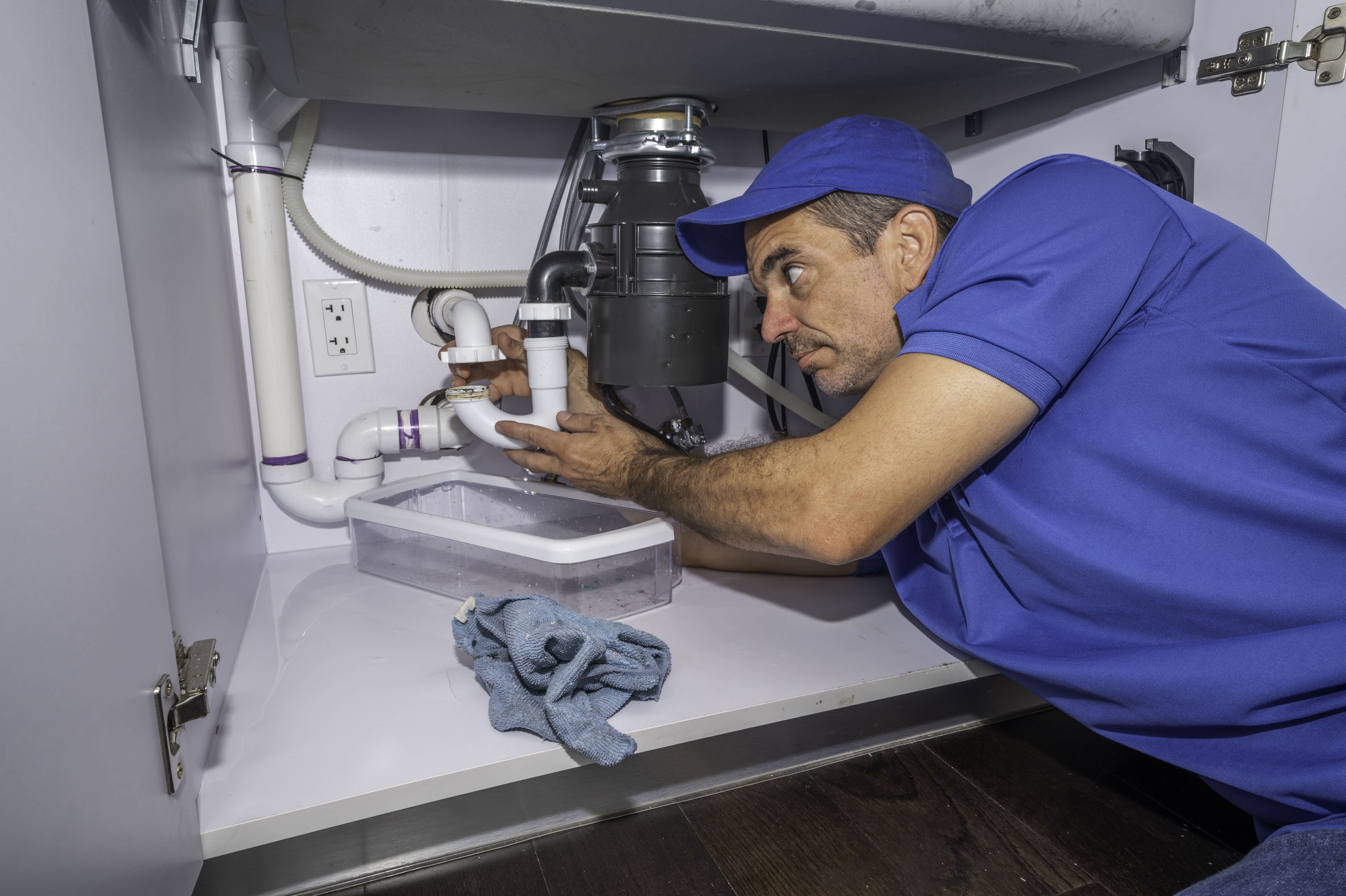 Plumber installing a garbage disposal under the sink