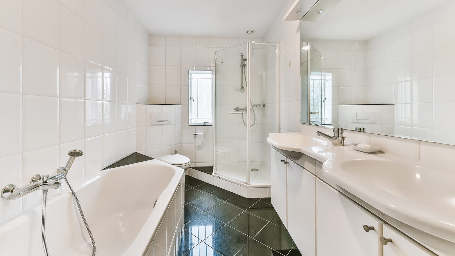A beautiful big white bathroom with black floor tiling