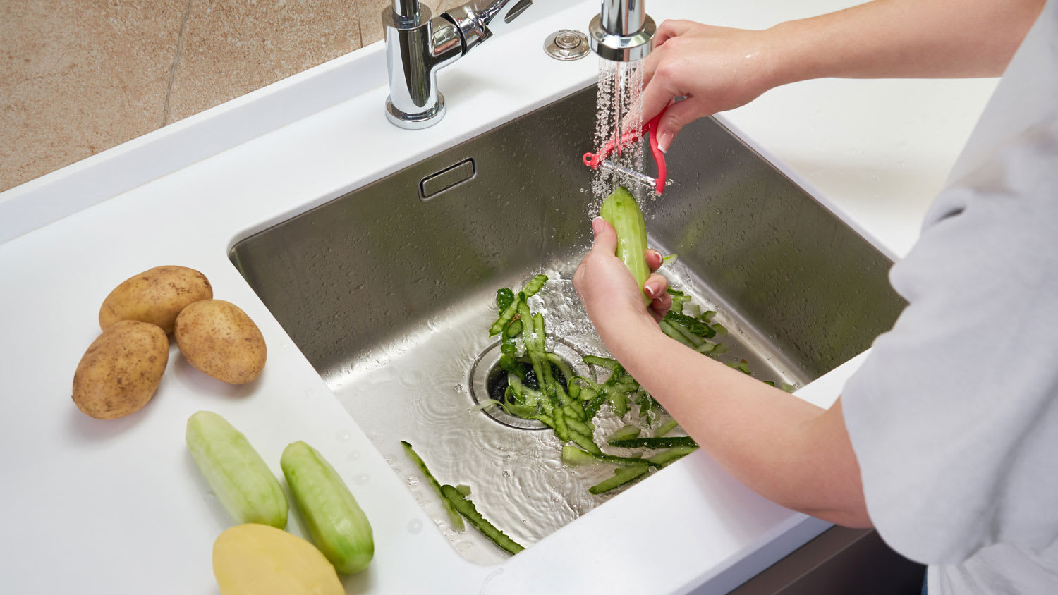 A woman cleaning a cucumber above a sink’s garbage disposal