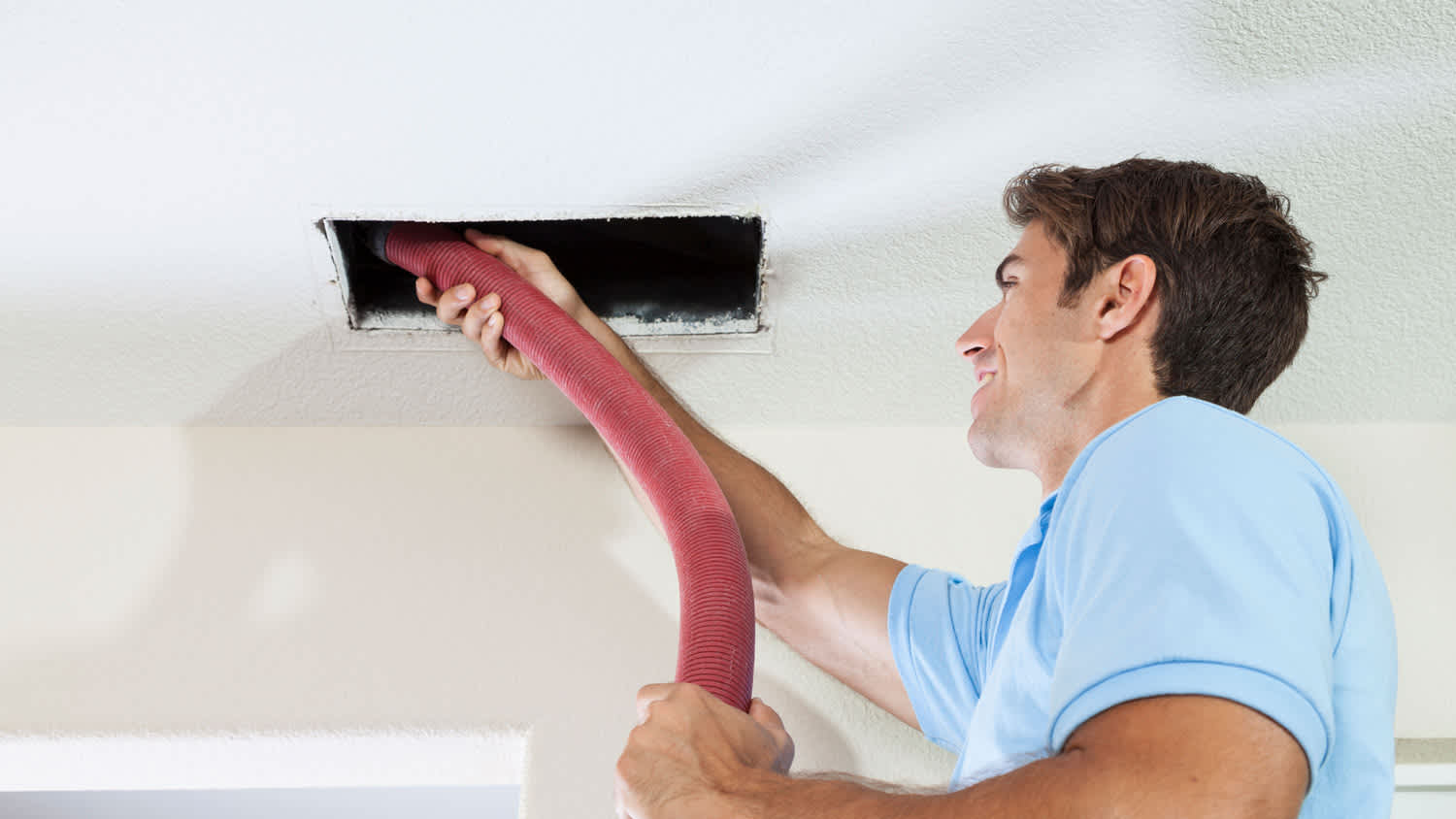 A man cleaning an air duct by using a vacuum cleaner