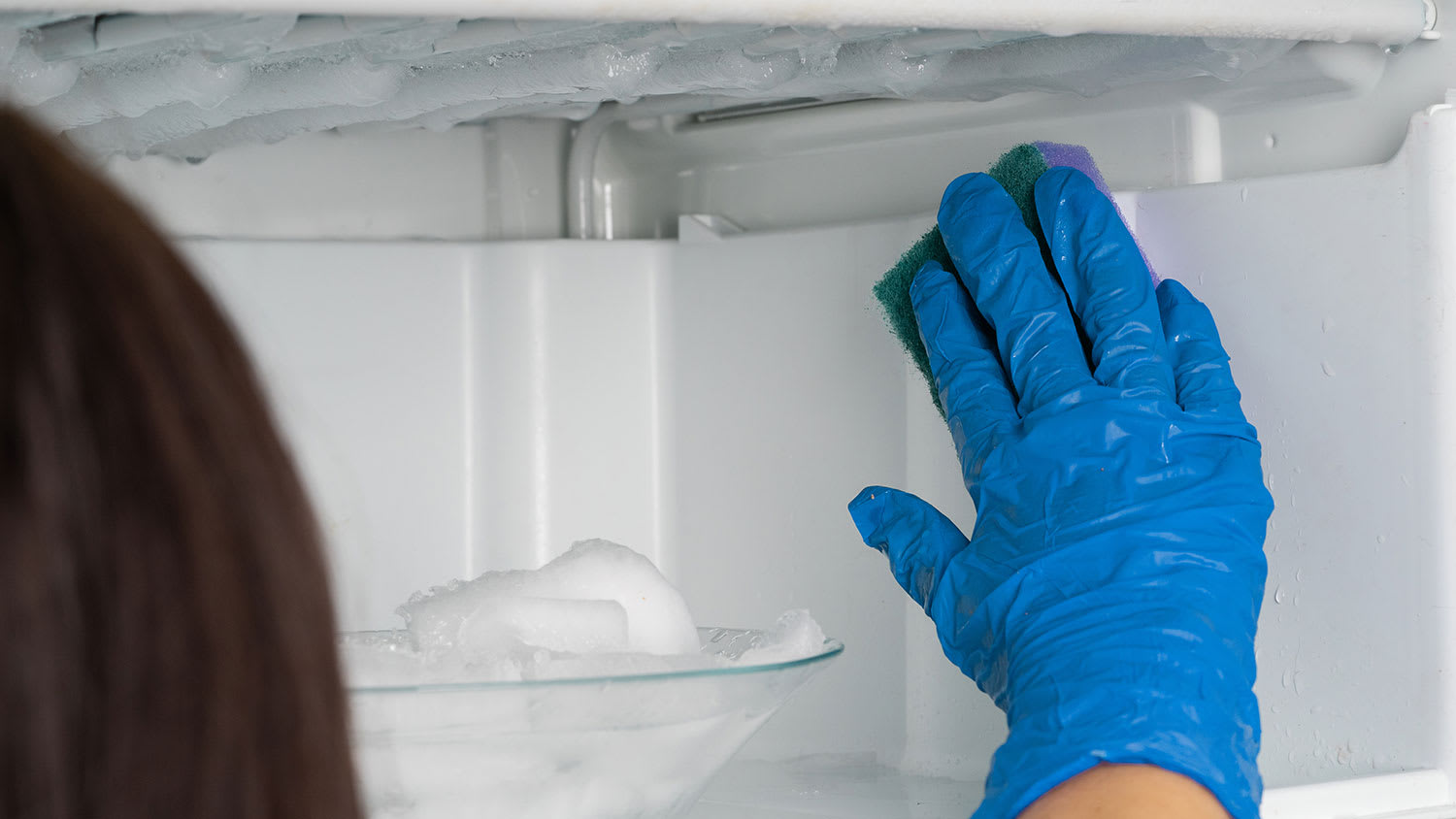 Woman wearing rubber gloves cleaning the freezer
