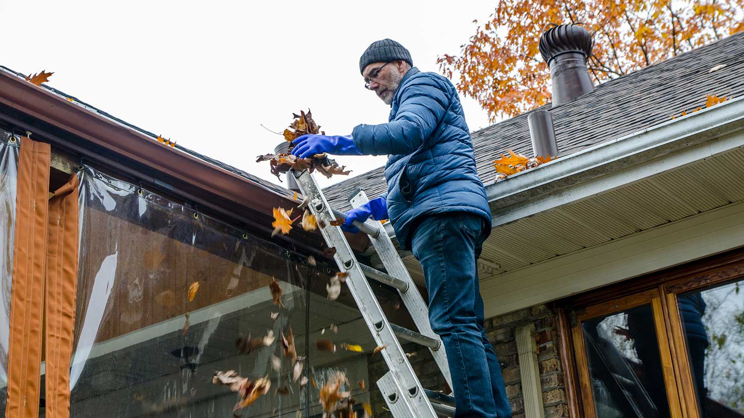 Man on a ladder removing leaves from gutters