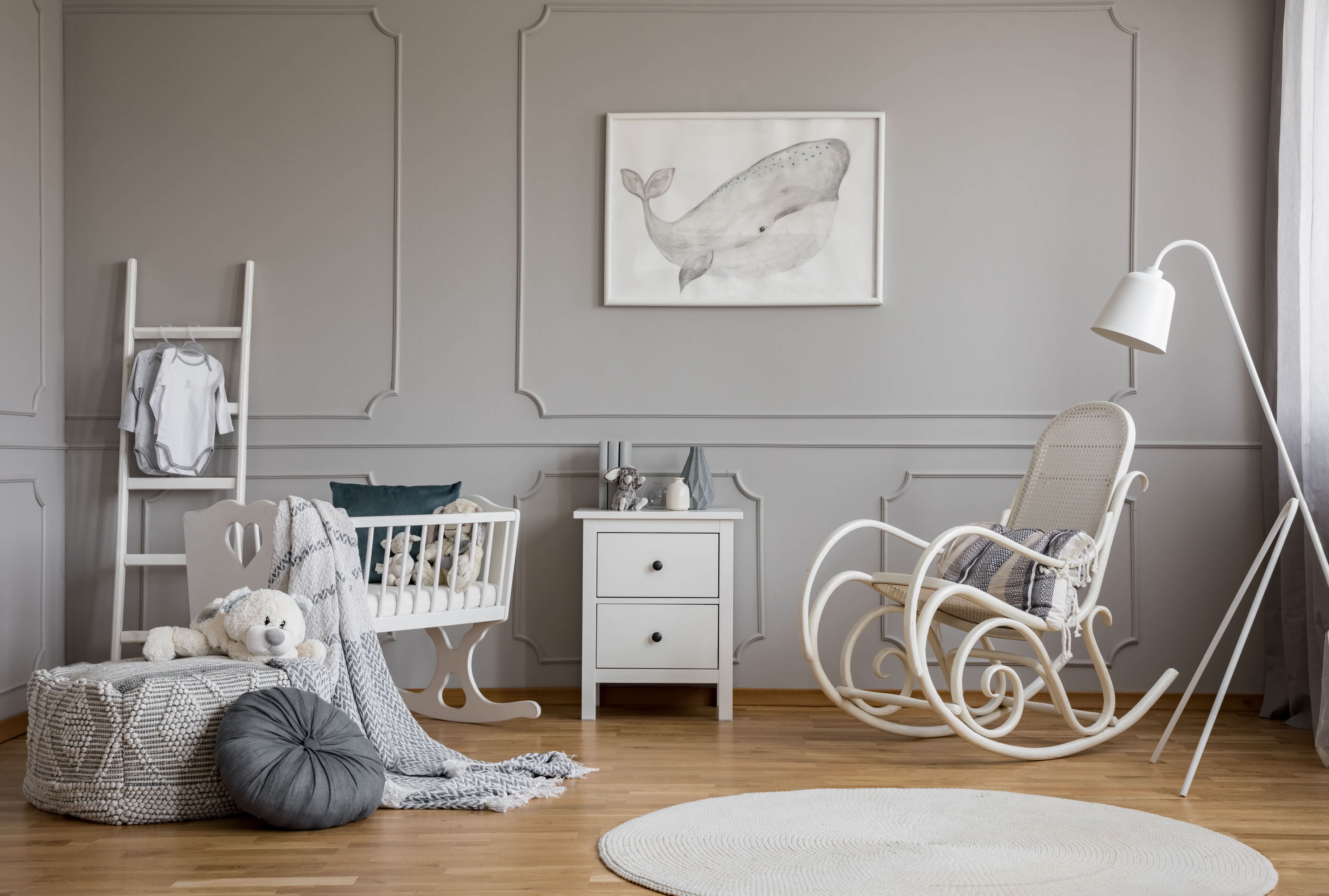 Baby nursery with white rocking chair, white and gray rug, and natural basket