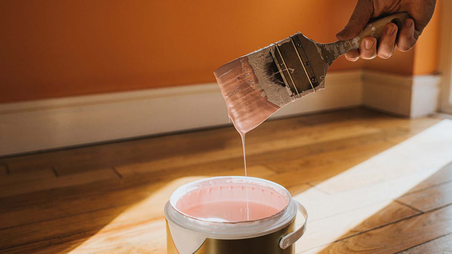 A hand holding a paint brush dipped in pink paint