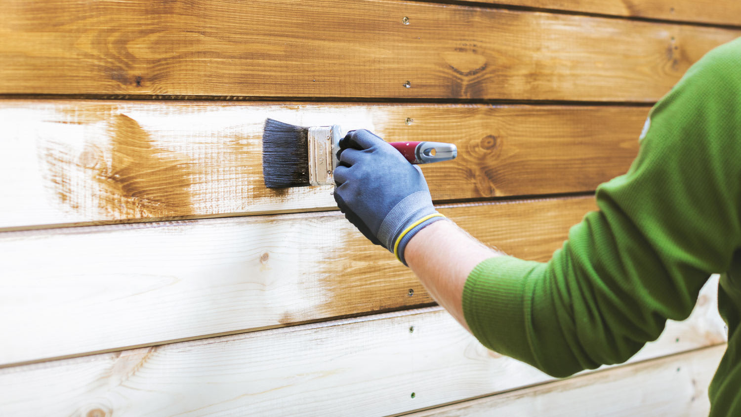 A man painting the wood siding with protective paint