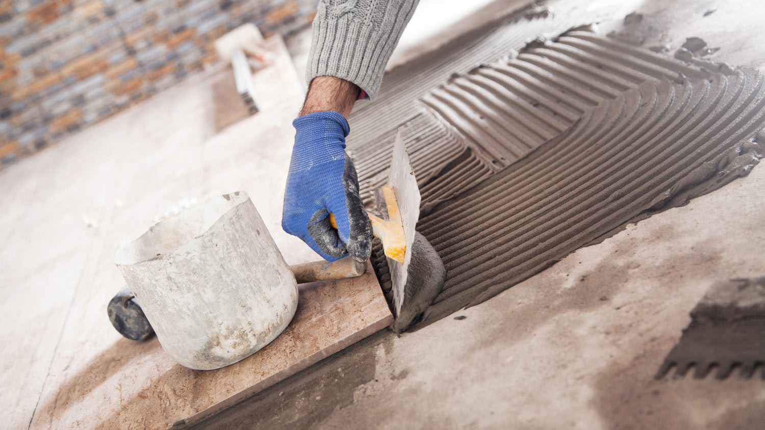 A worker laying tiles while using a notched trowel