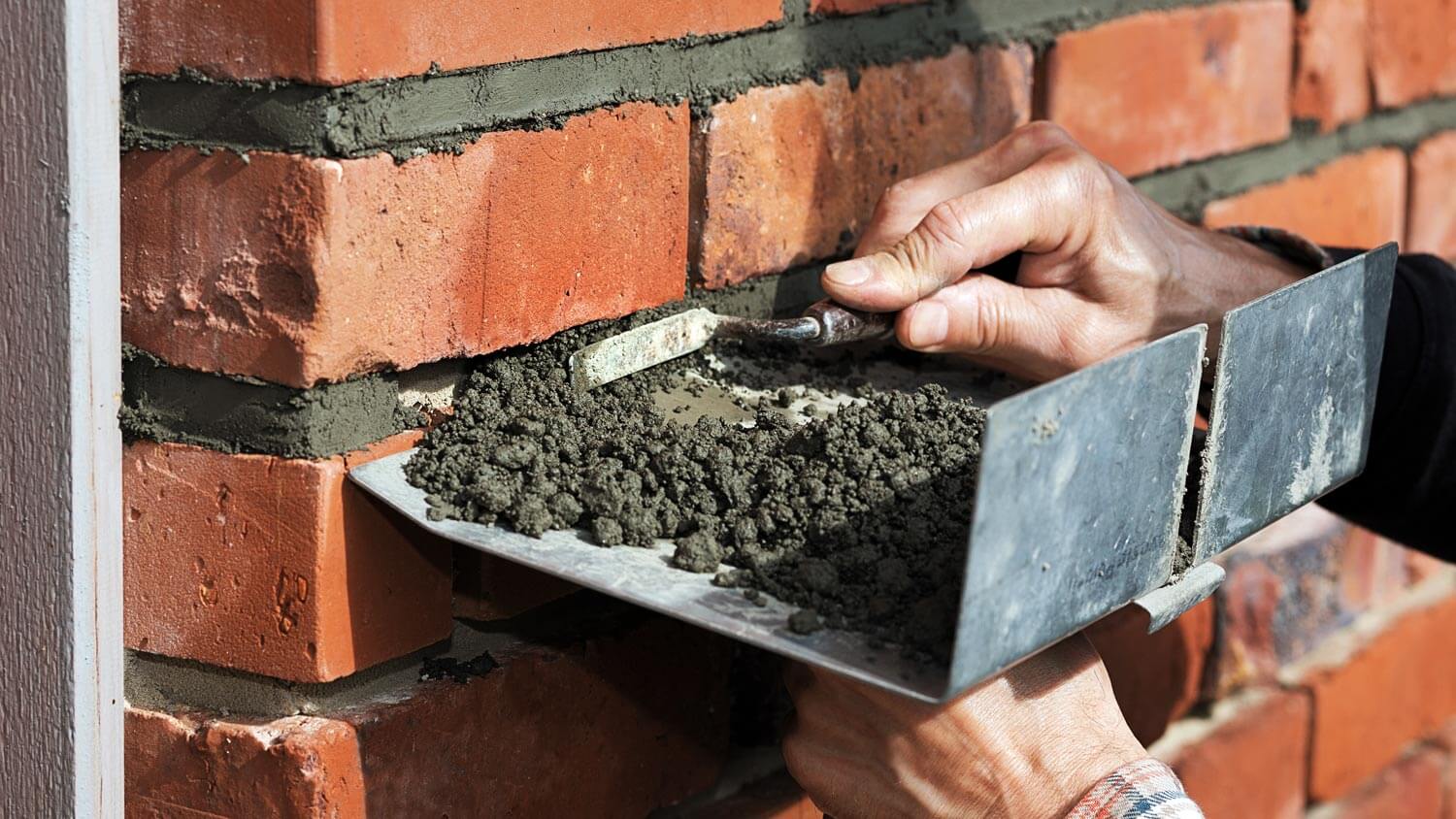 A worker replacing mortar holding bricks together