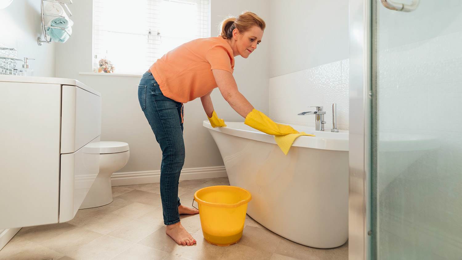 Woman cleans her deep bathtub with a cloth