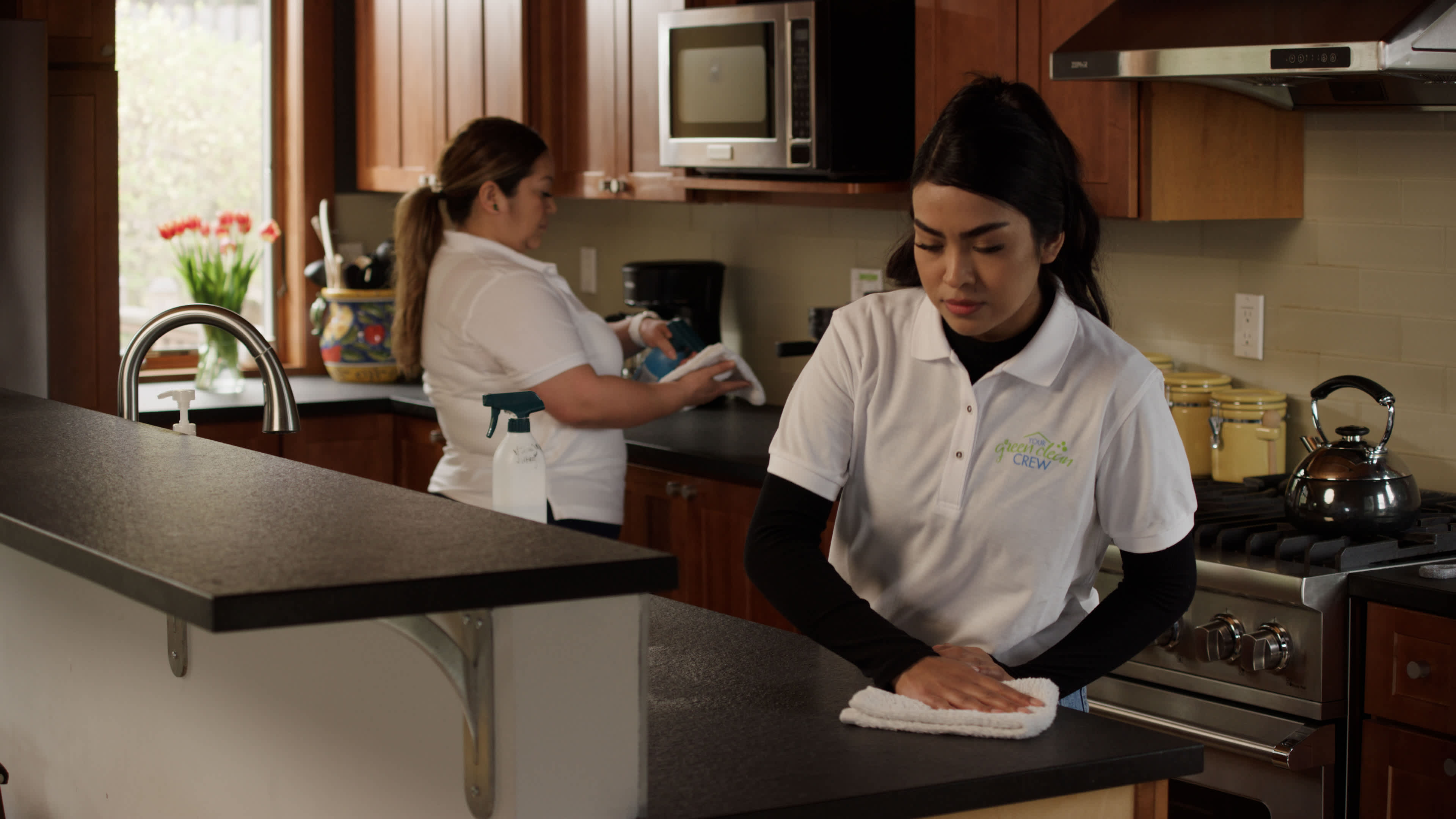 Two women clean kitchen countertops
