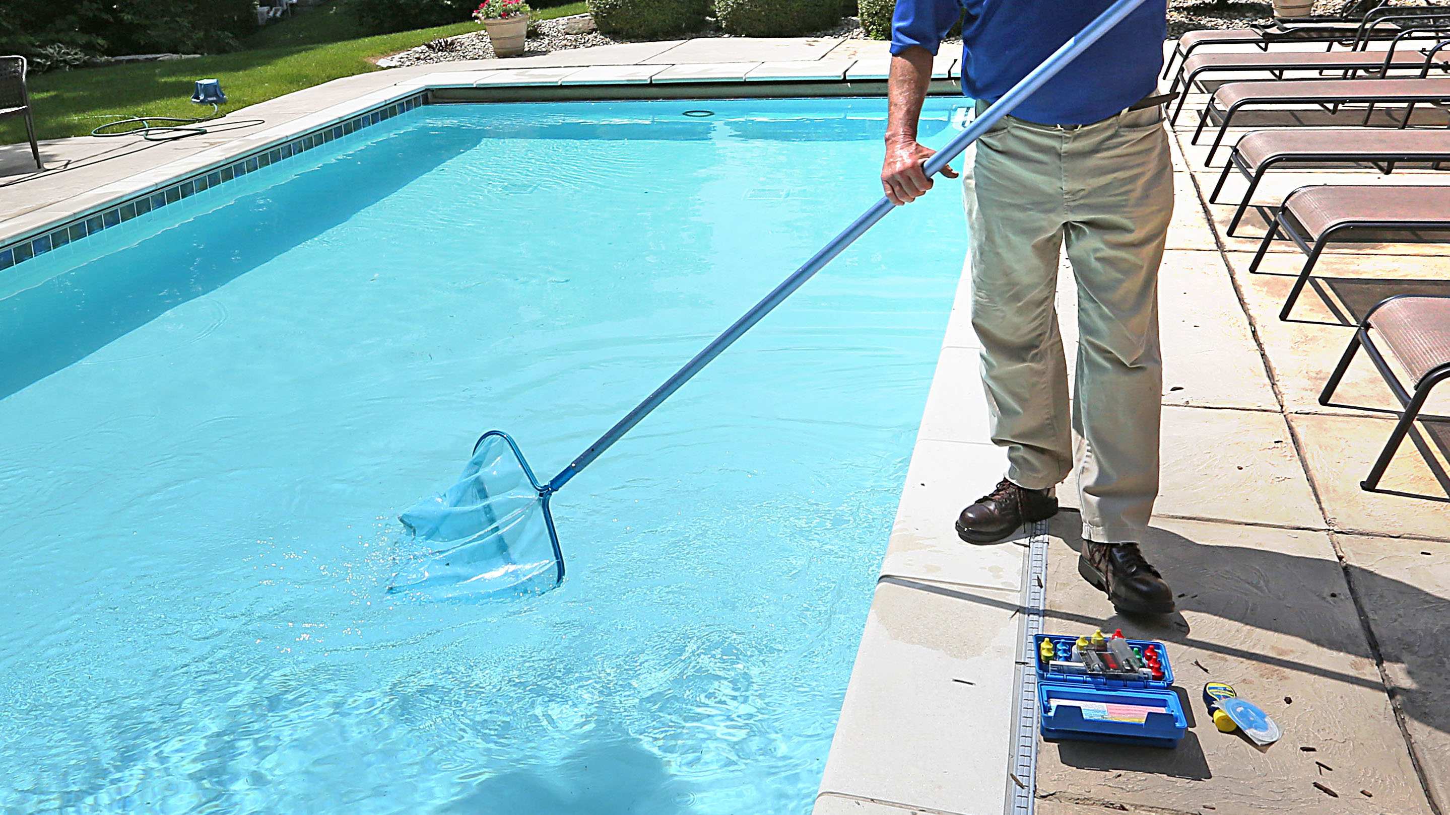 A man removes debris from a swimming pool with a skim net.