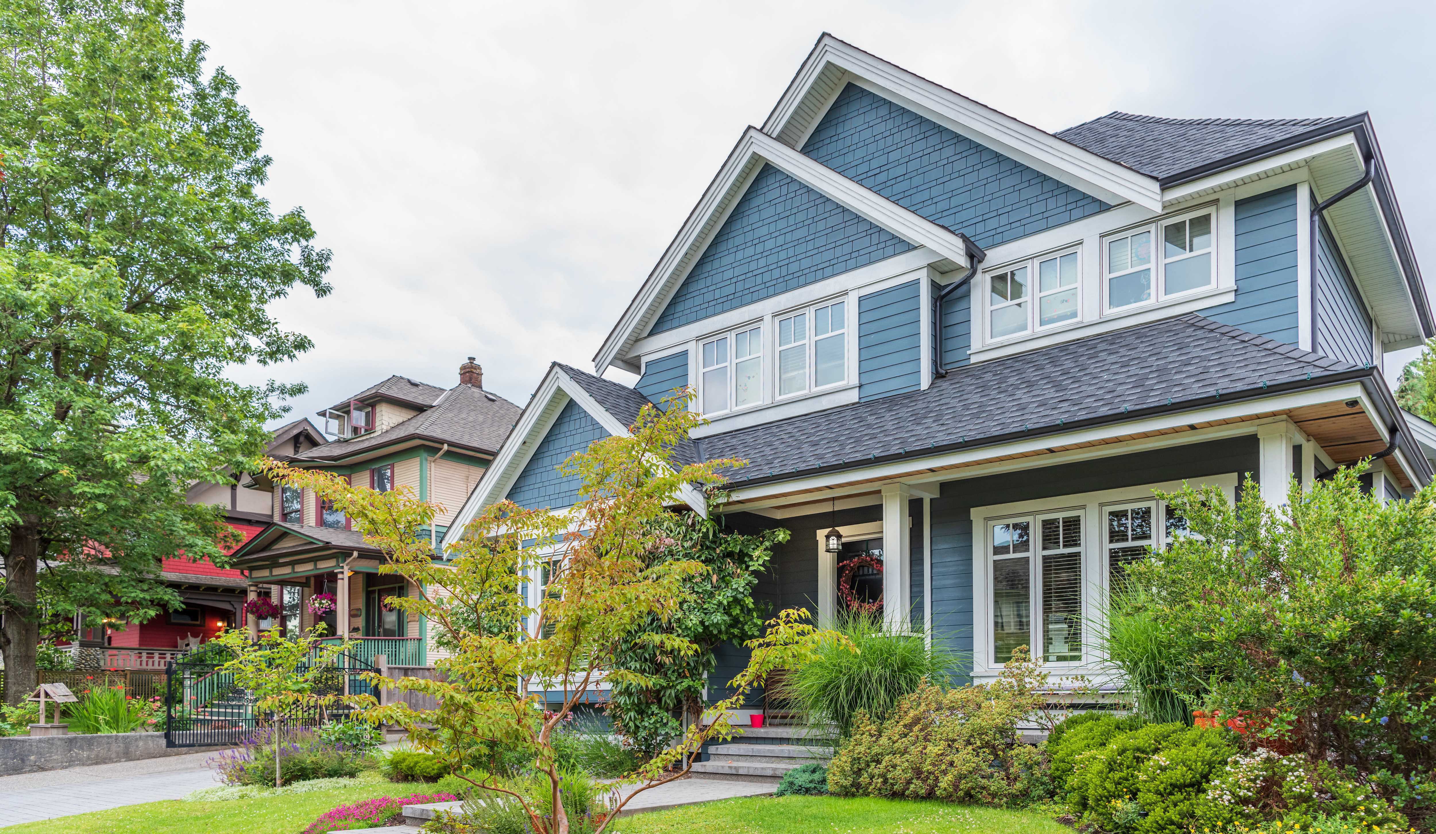 A blue luxury suburban house with gray roof and white trim and green landscaping