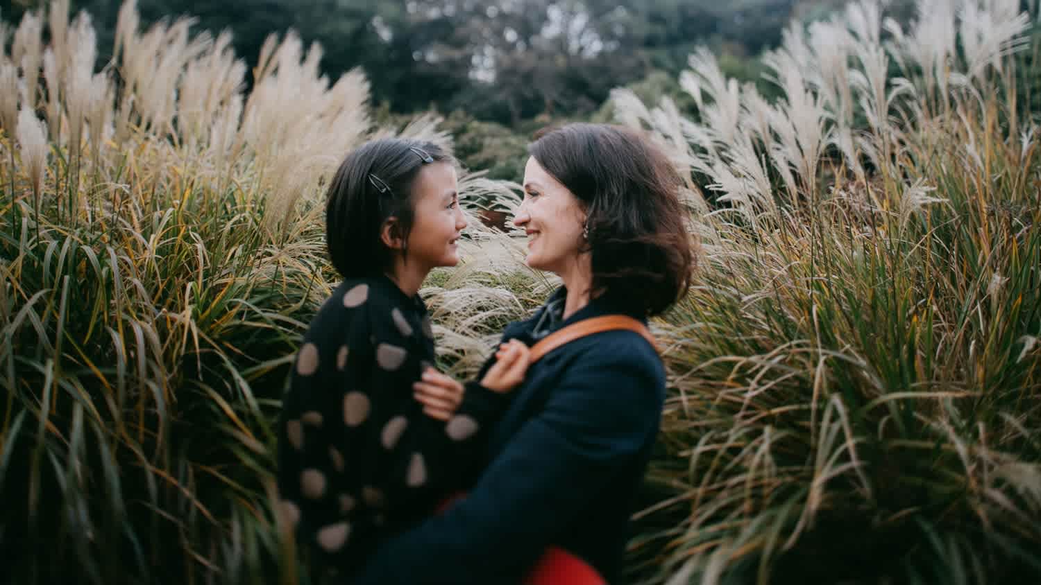 A mother and her daughter cuddling surrounded by pampas grass