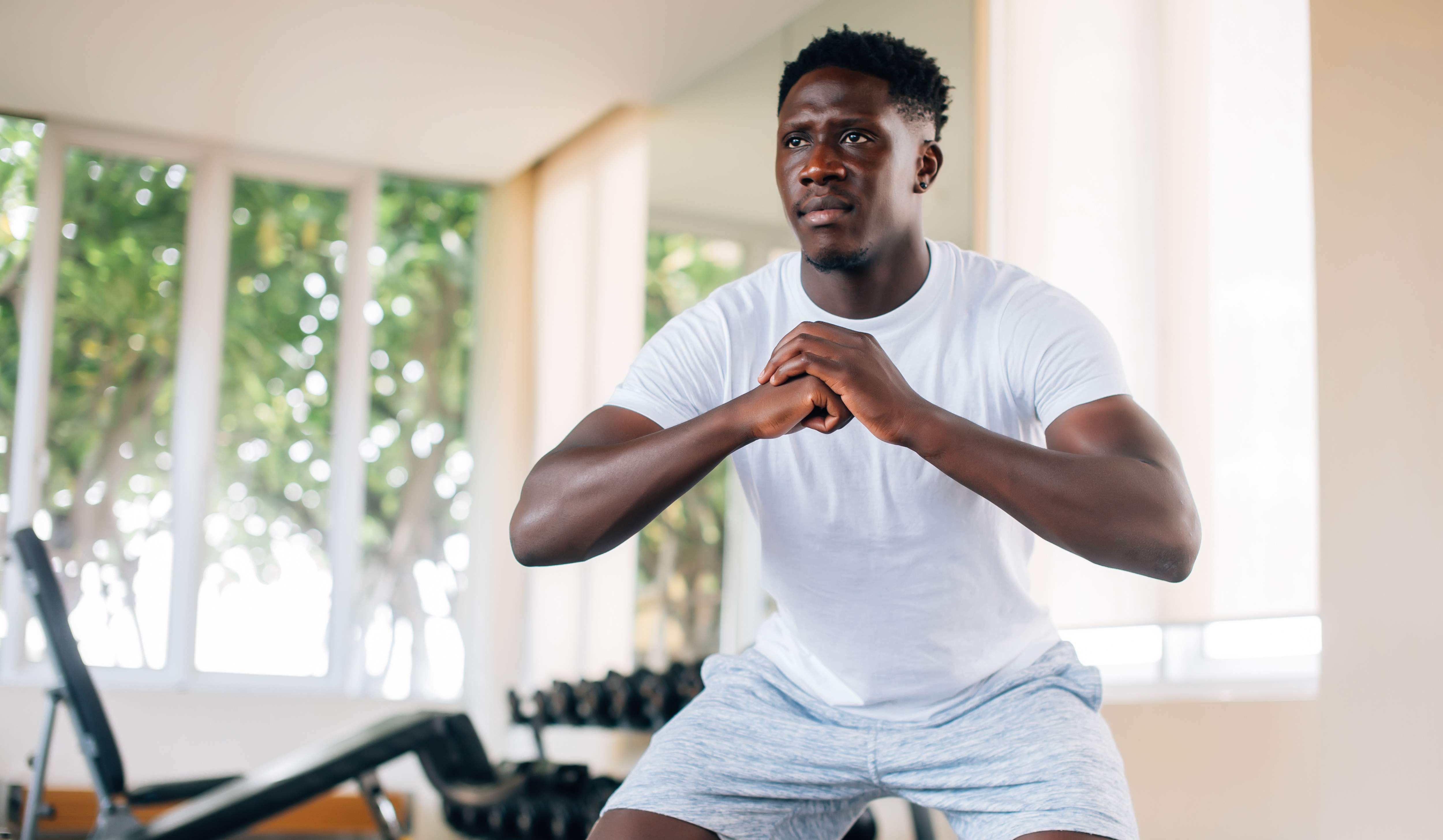 An African American man in a white shirt doing squats in his home gym