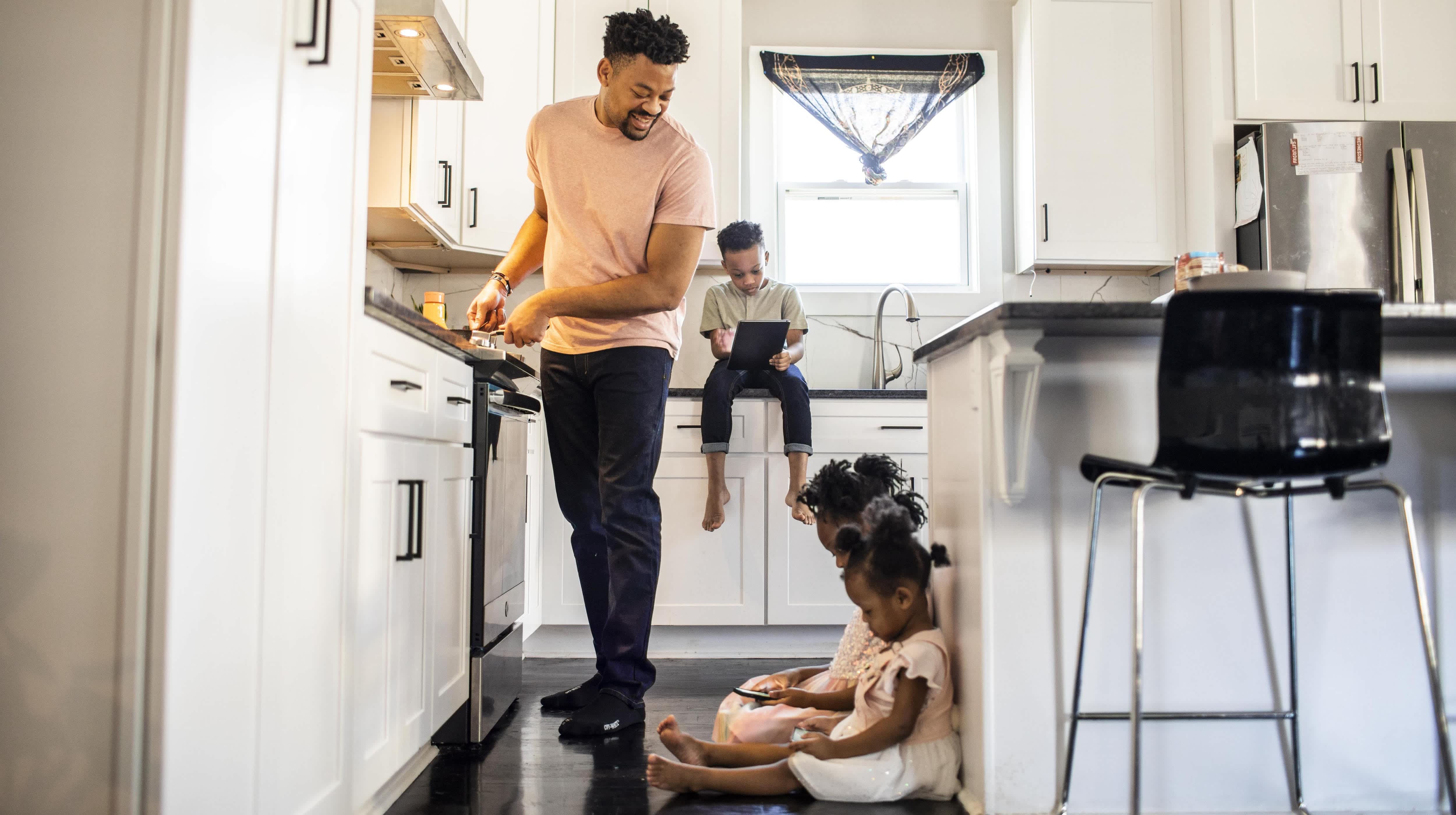 Father cooking breakfast while his three young kids hang out in the kitchen