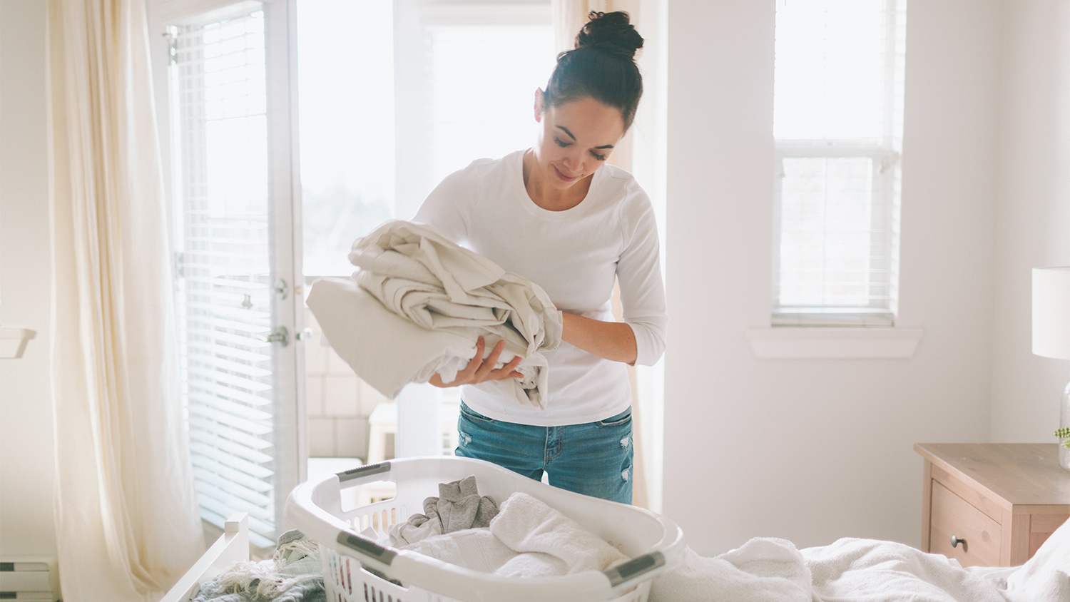 woman folding white laundry in bedroom