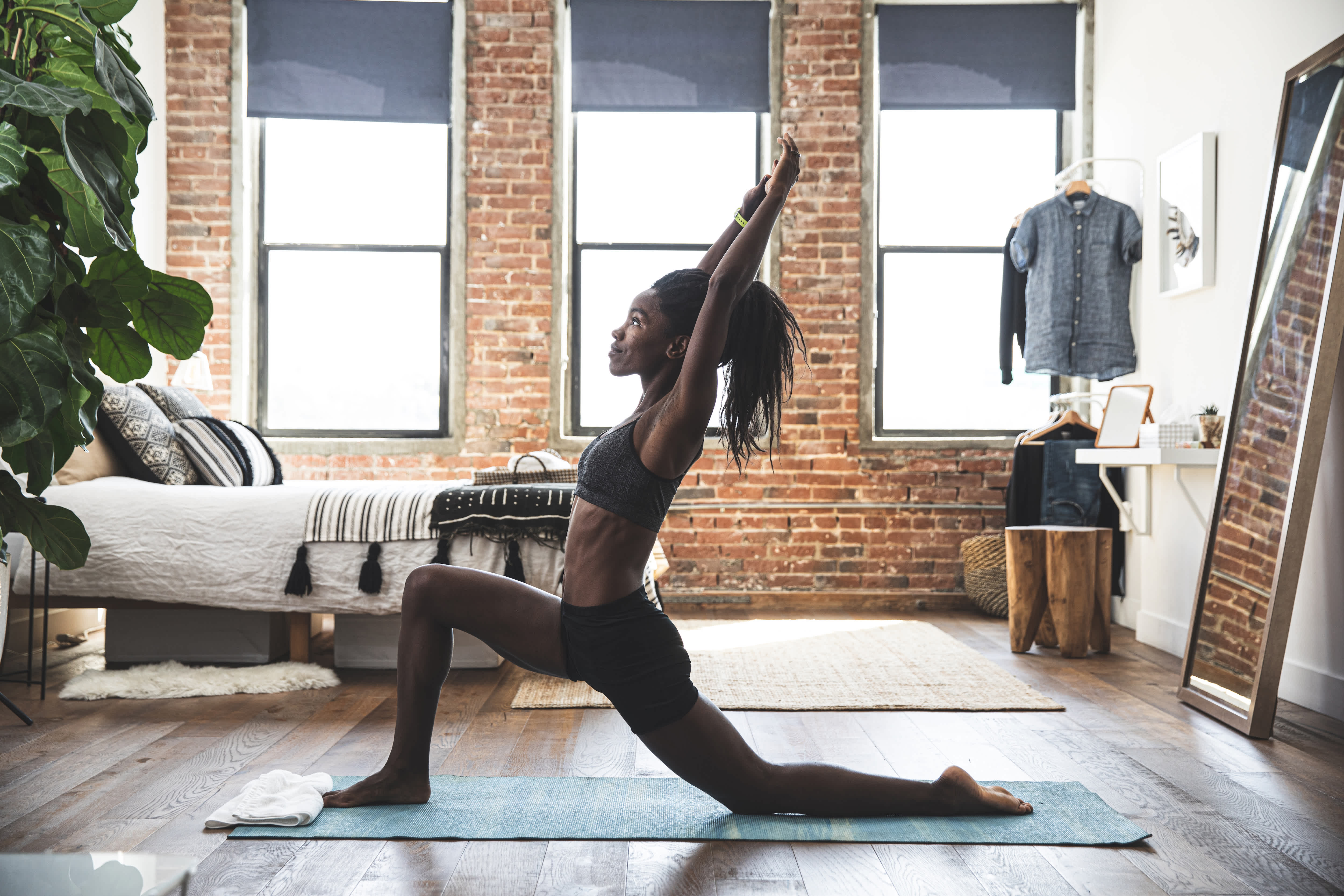 Young woman in gray yoga clothes doing yoga in her bedroom with a turquoise yoga mat with a white towel