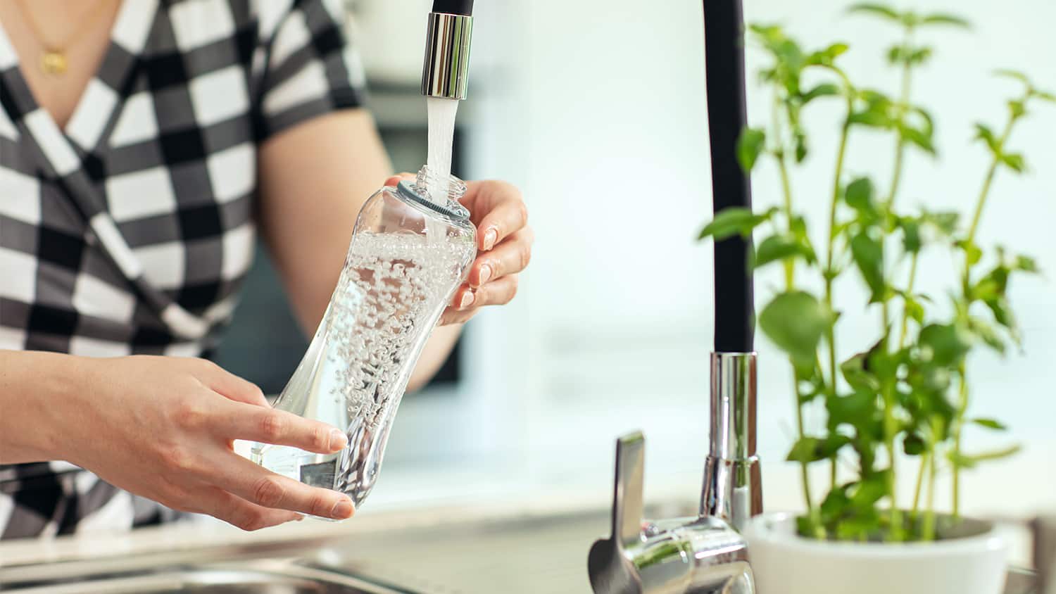 woman filling up water bottle in sink