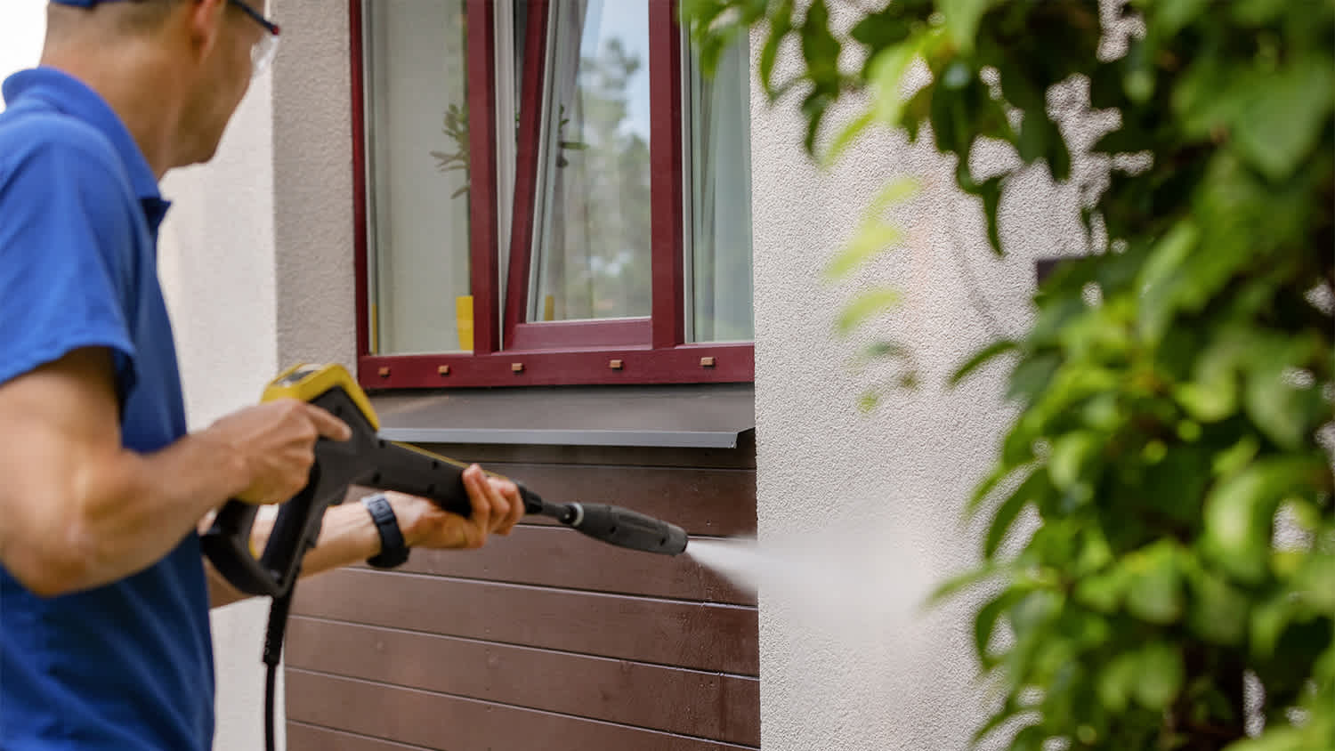 man using pressure washer to clean home exterior