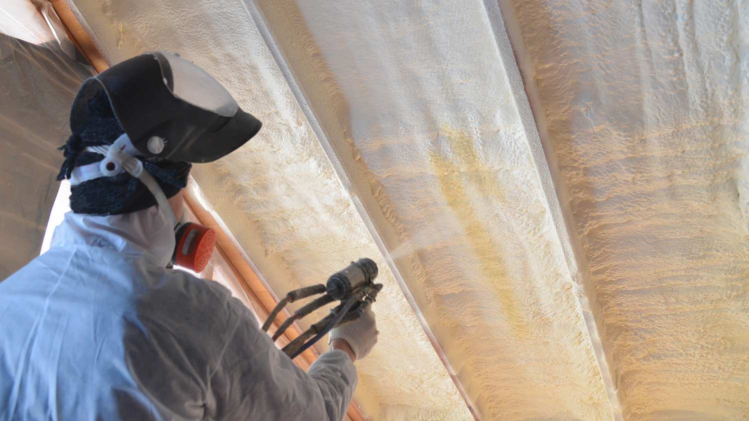 worker spraying warming coat on attic walls