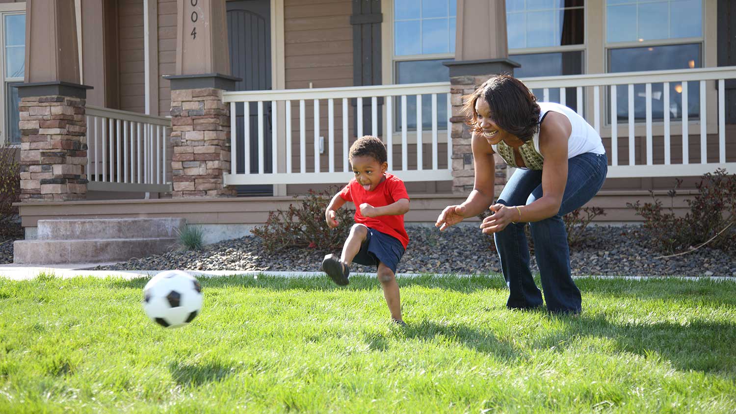 Boy playing soccer with mom in the front yard
