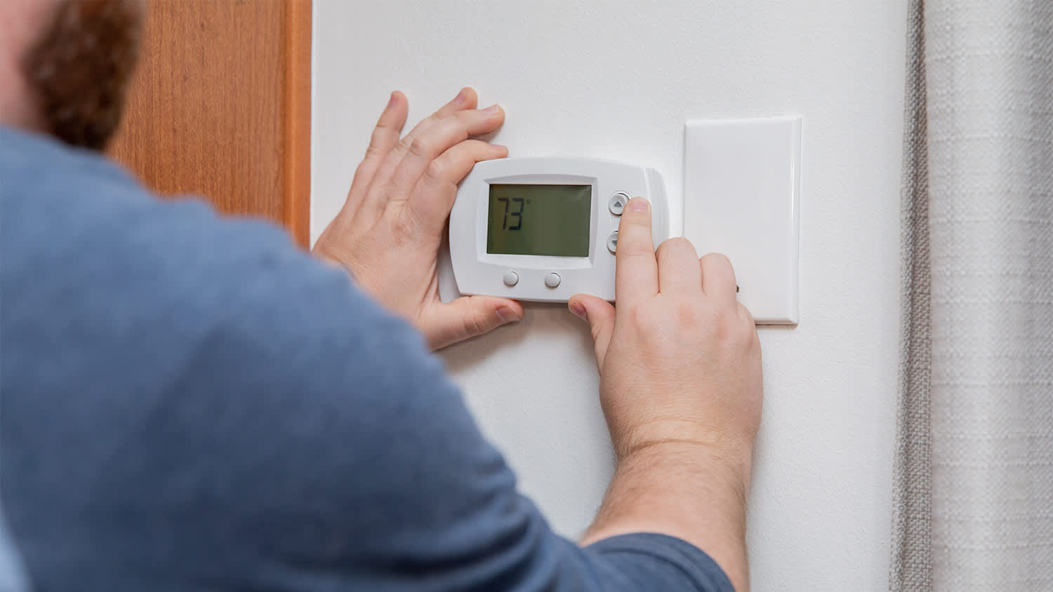 A man changing the temperature via a thermostat