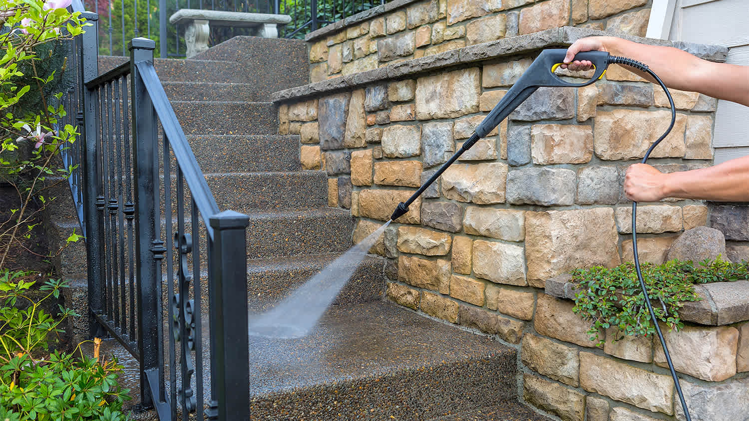 man using pressure power washer to clean steps