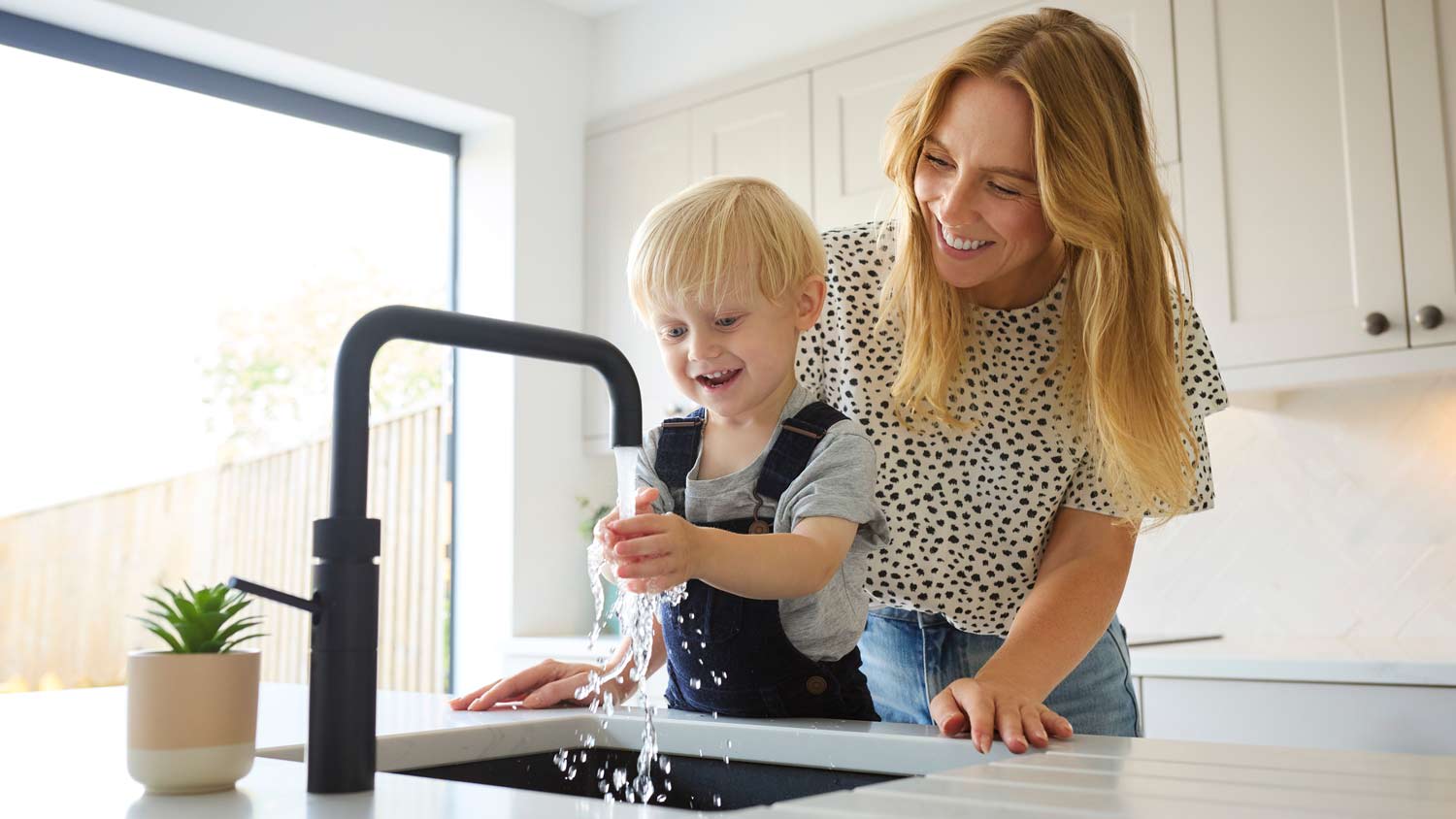 mother watching child wash hands in kitchen